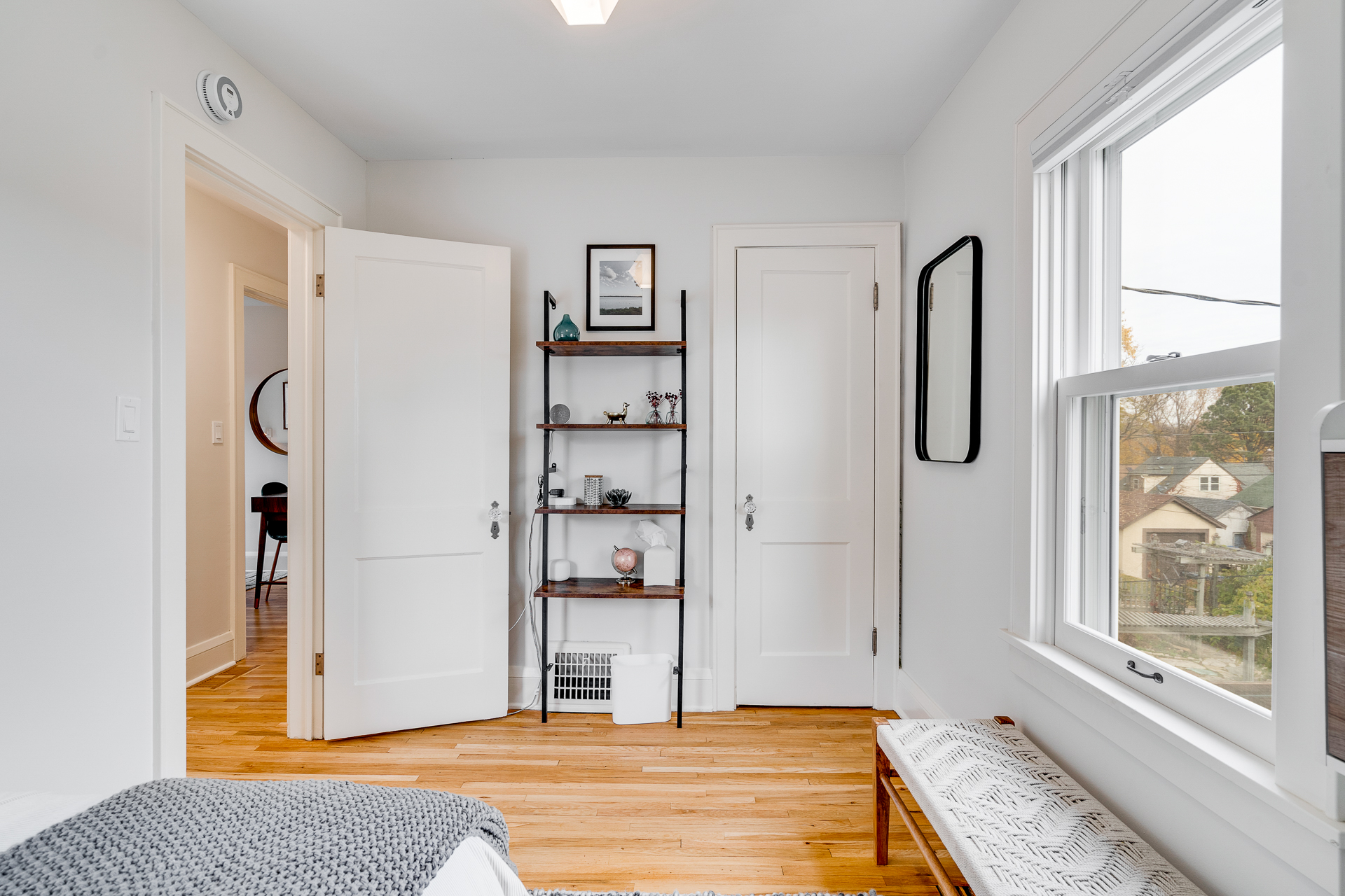 A bright and minimalistic room featuring a decorative shelf, a bench, and natural light.
