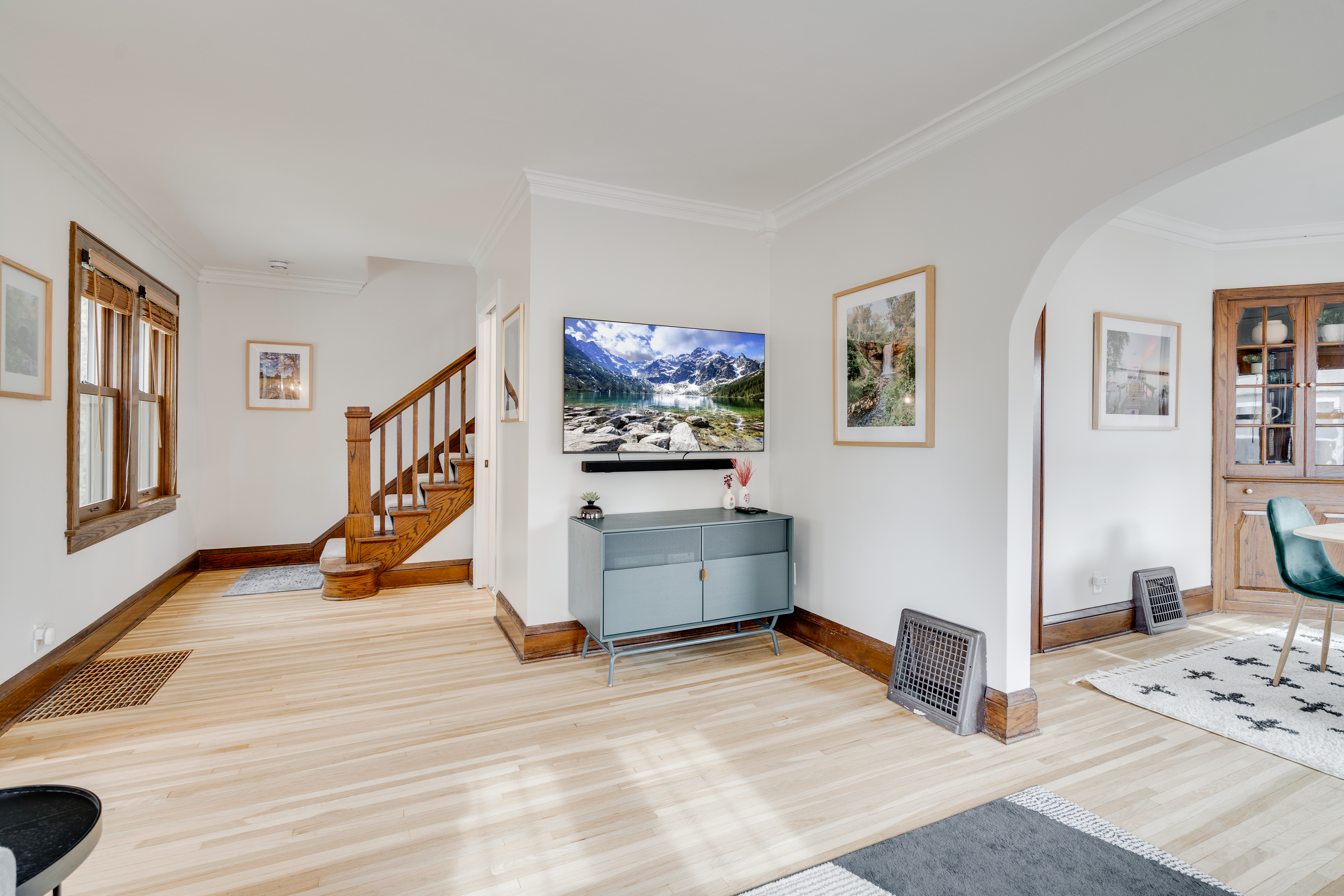 A bright and inviting living room featuring a staircase, a media console with a television, and a dining area.