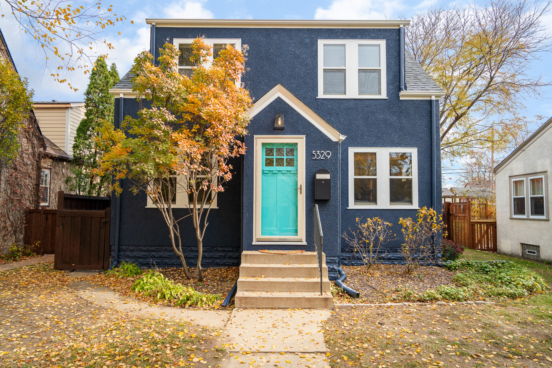 A cozy navy blue house with a bright turquoise door, surrounded by autumn foliage.