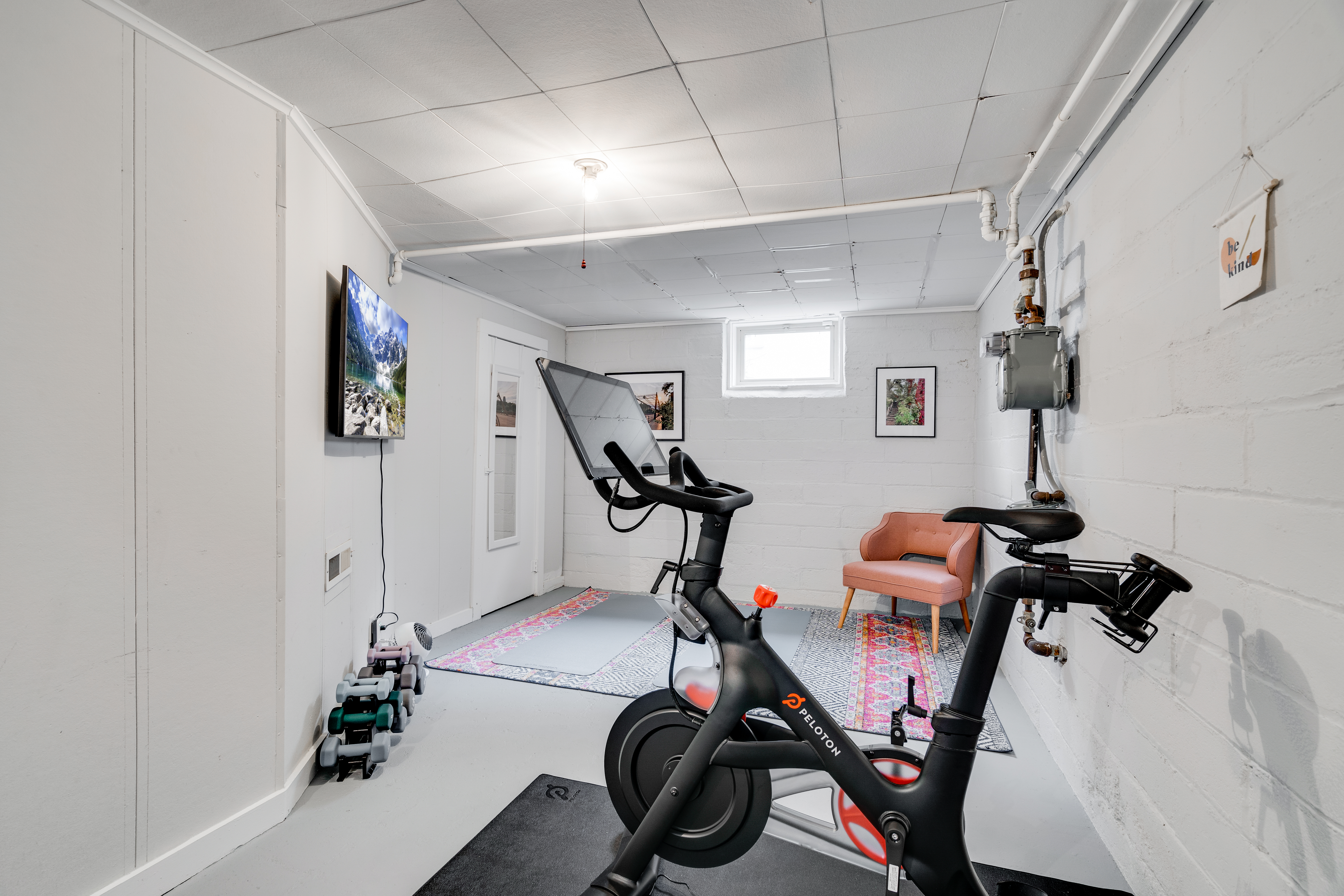 A modern basement fitness space featuring a Peloton bike, weights, and cozy seating.
