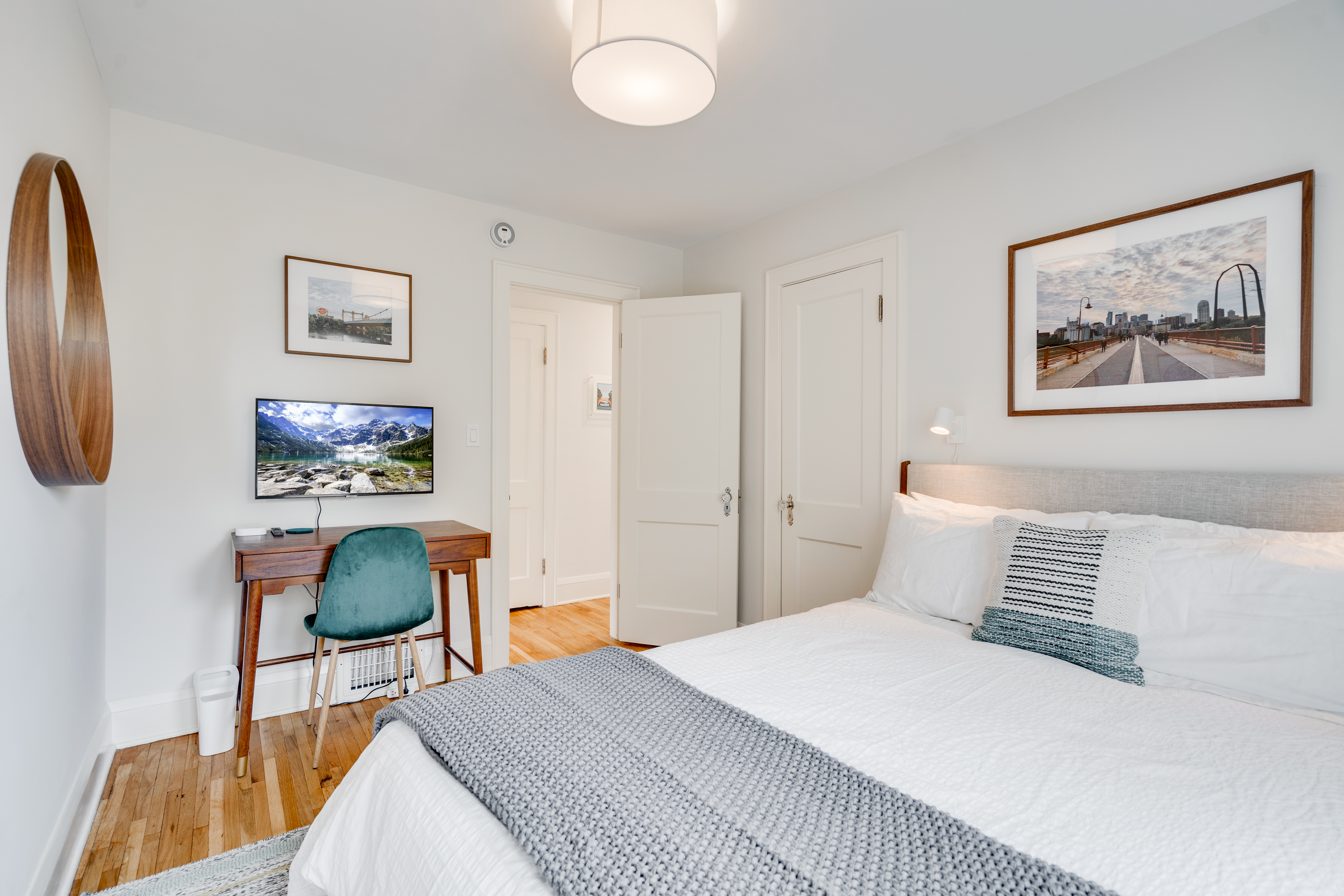 A modern bedroom featuring a cozy bed, a wooden desk, and framed photographs.