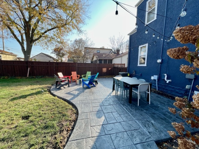 A colorful outdoor space with adirondack chairs and a dining table, surrounded by a well-manicured lawn.
