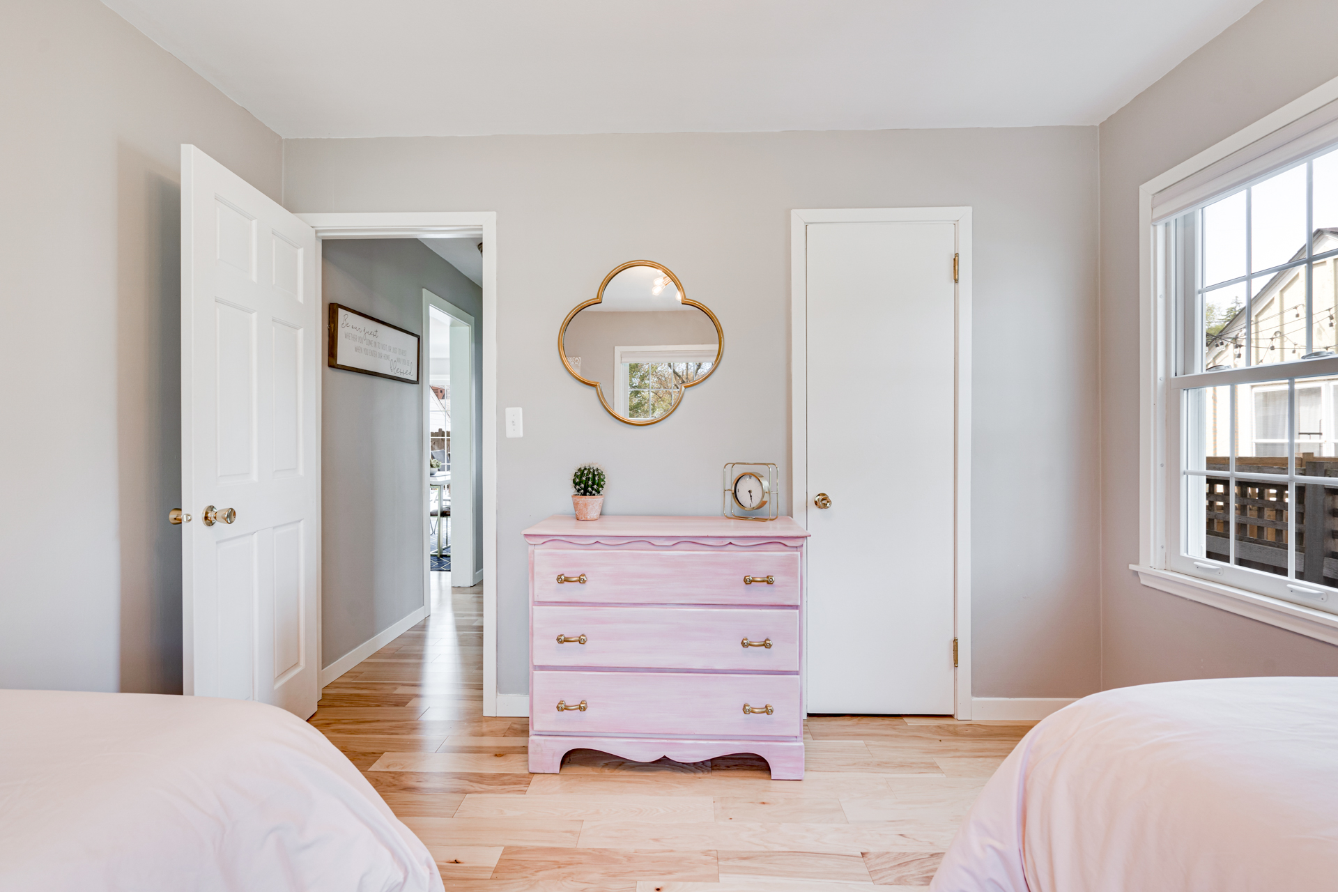 A cozy pastel-themed bedroom featuring a pink dresser and natural light.