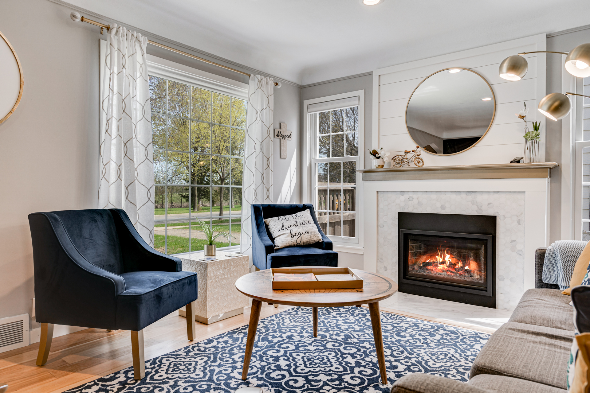 A stylish living room with blue chairs, a round coffee table, and a fireplace.