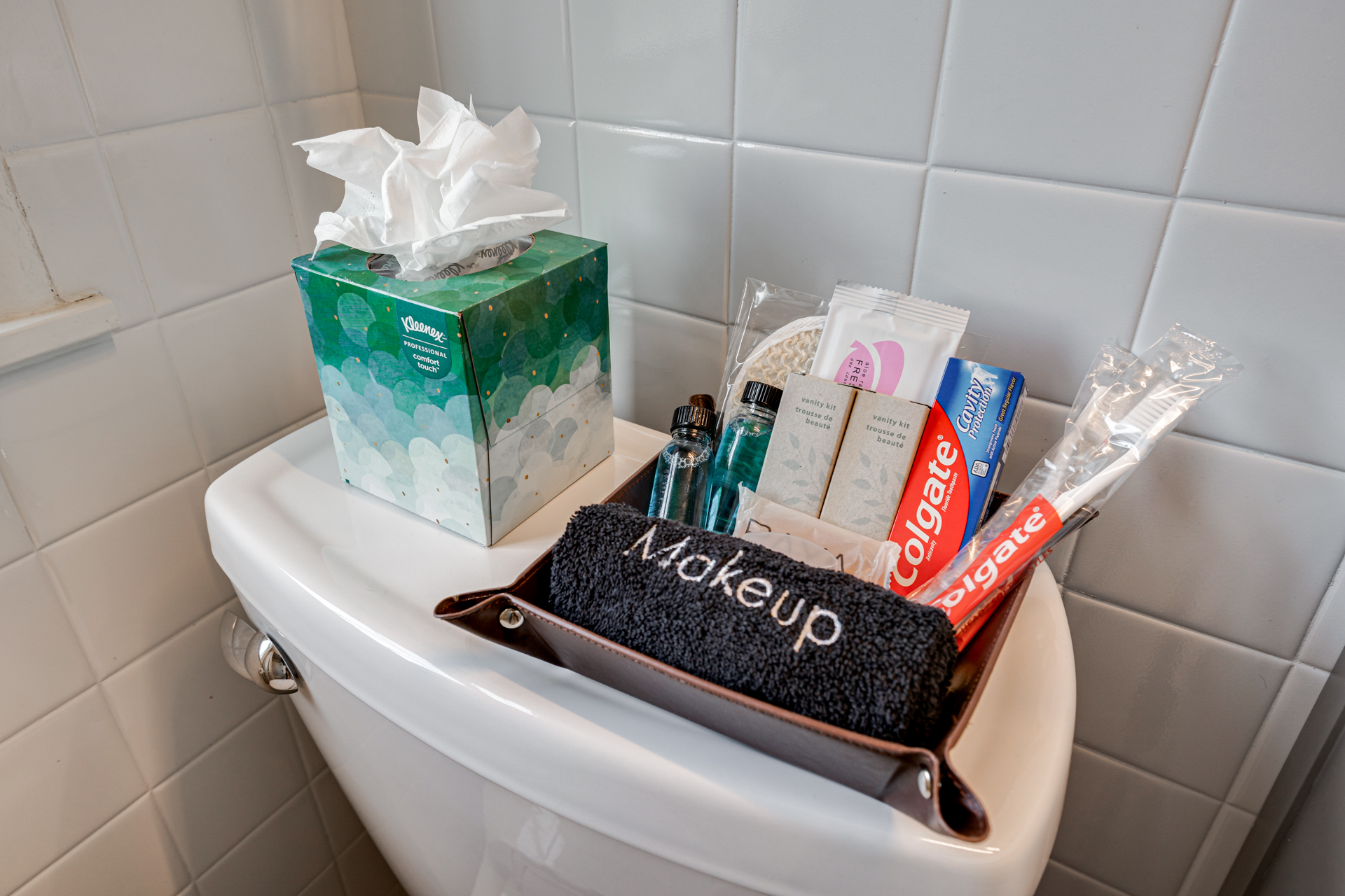A collection of personal care items arranged on a toilet lid, featuring a makeup towel and various essentials.