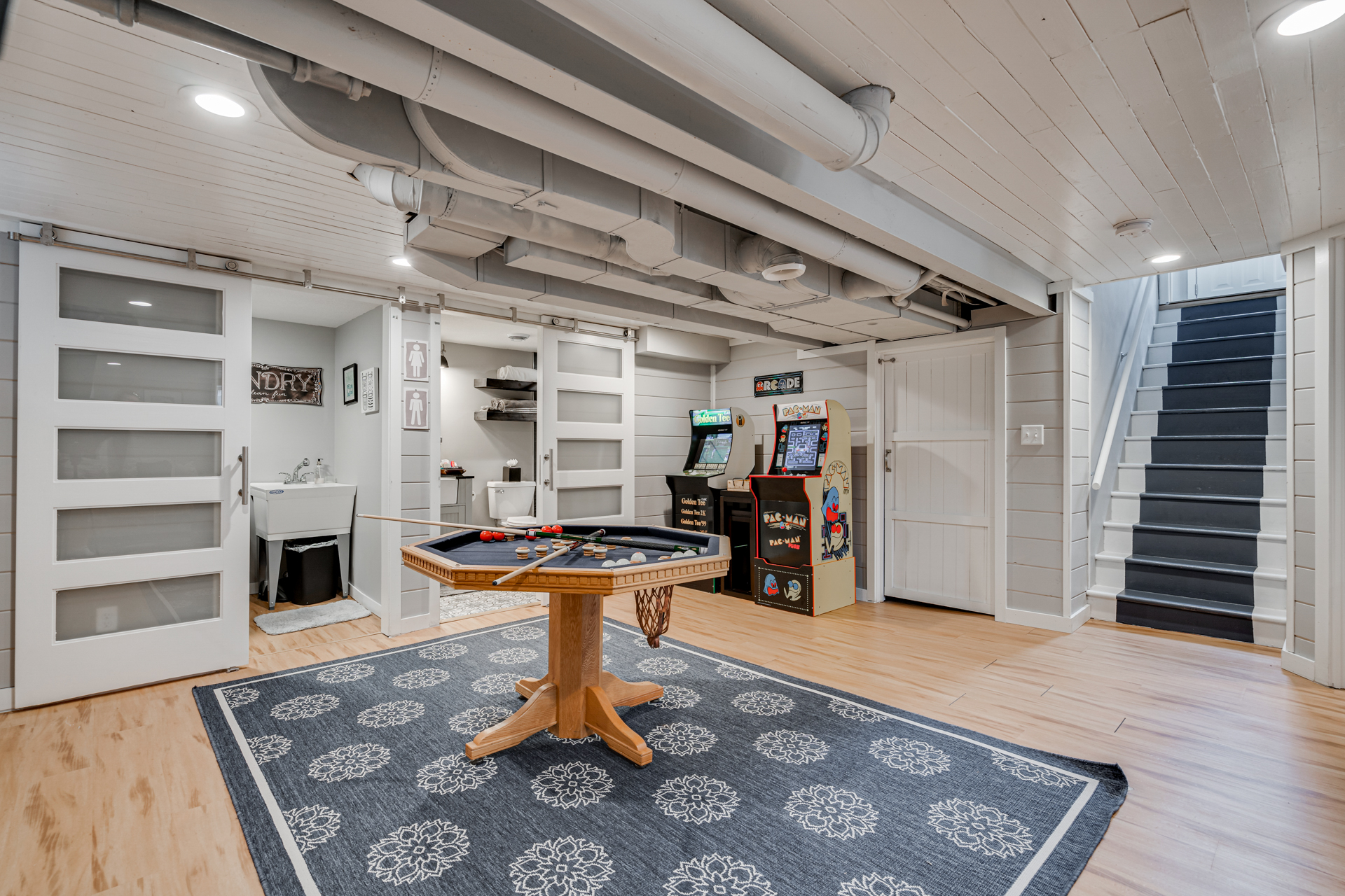 A cozy basement recreation room featuring a pool table and arcade games.