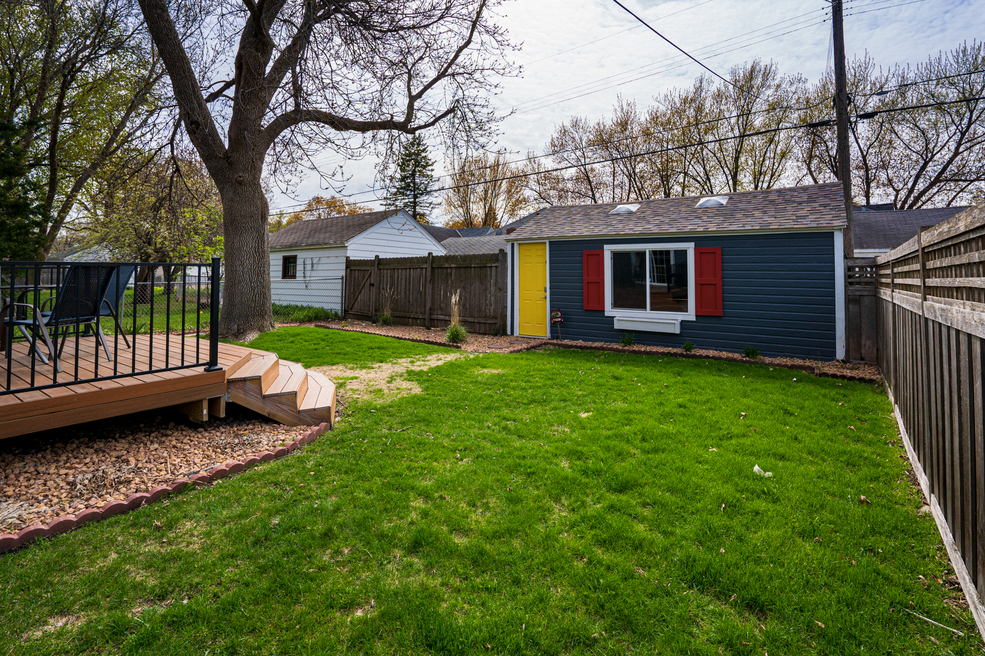 A peaceful backyard featuring a blue shed, a wooden deck, and lush greenery.