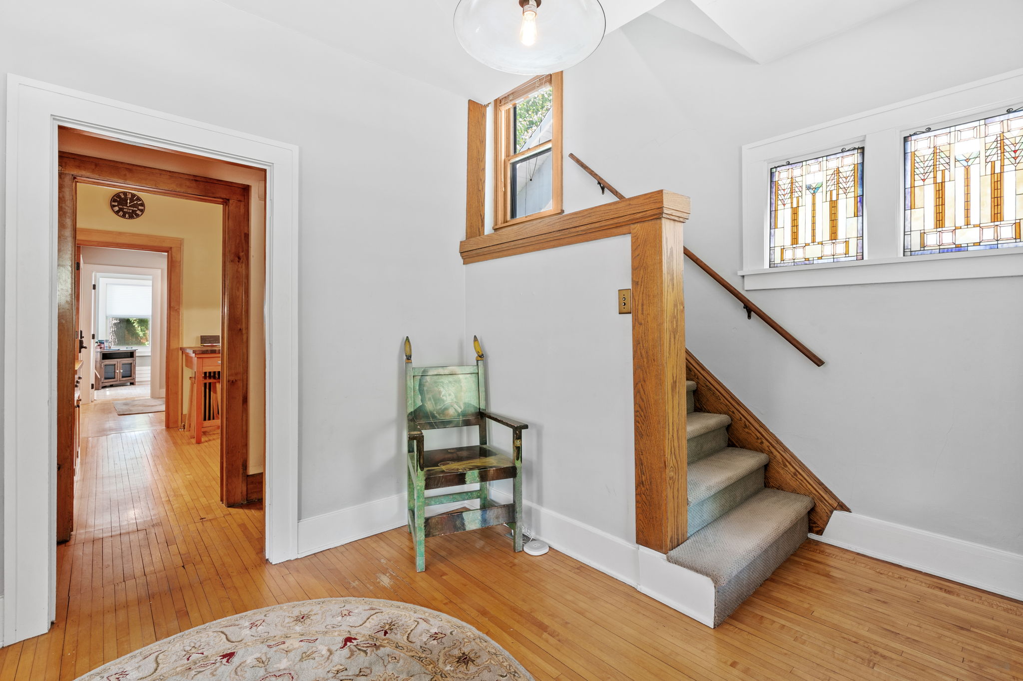 A welcoming entryway featuring a staircase, unique chair, and stained glass windows.