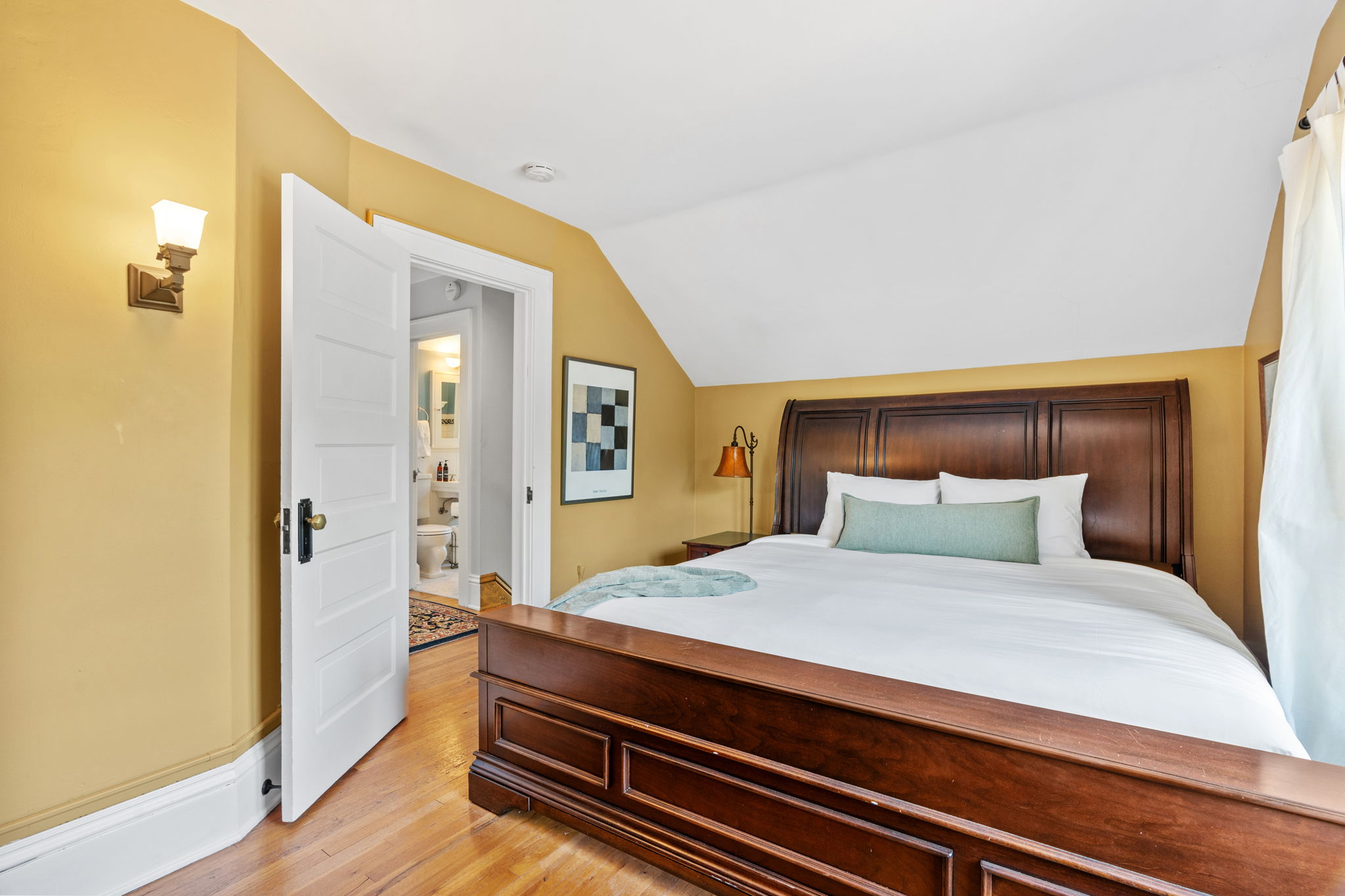 A cozy bedroom with warm tones and a wooden bed, featuring a glimpse into the adjoining bathroom.