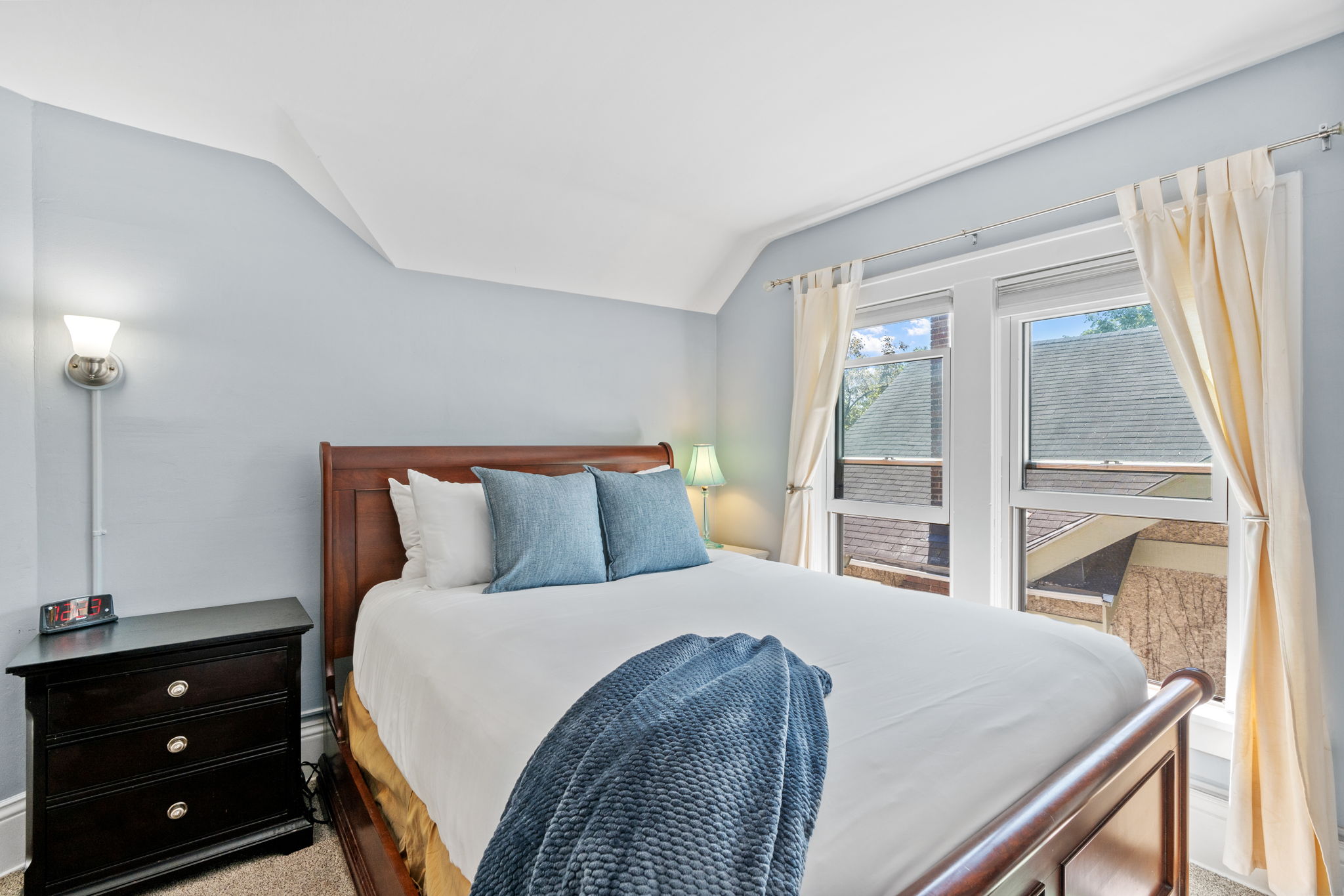 A serene bedroom with a wooden bed and blue accents, illuminated by natural light.