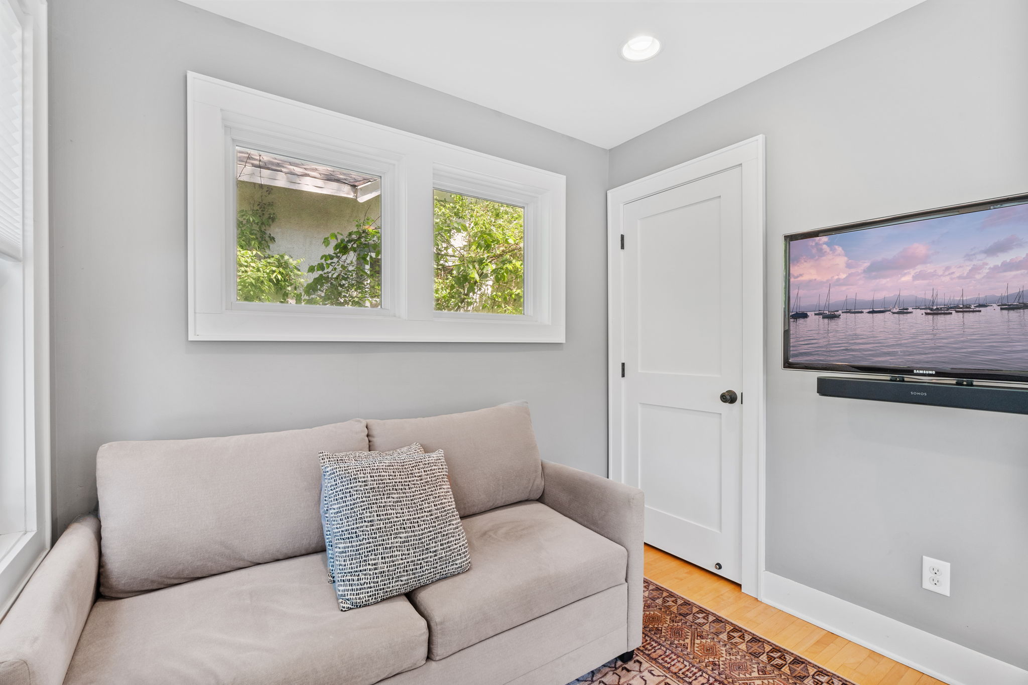 A modern living room corner featuring a cozy couch, large windows, and a flat-screen TV displaying a tranquil marina scene.