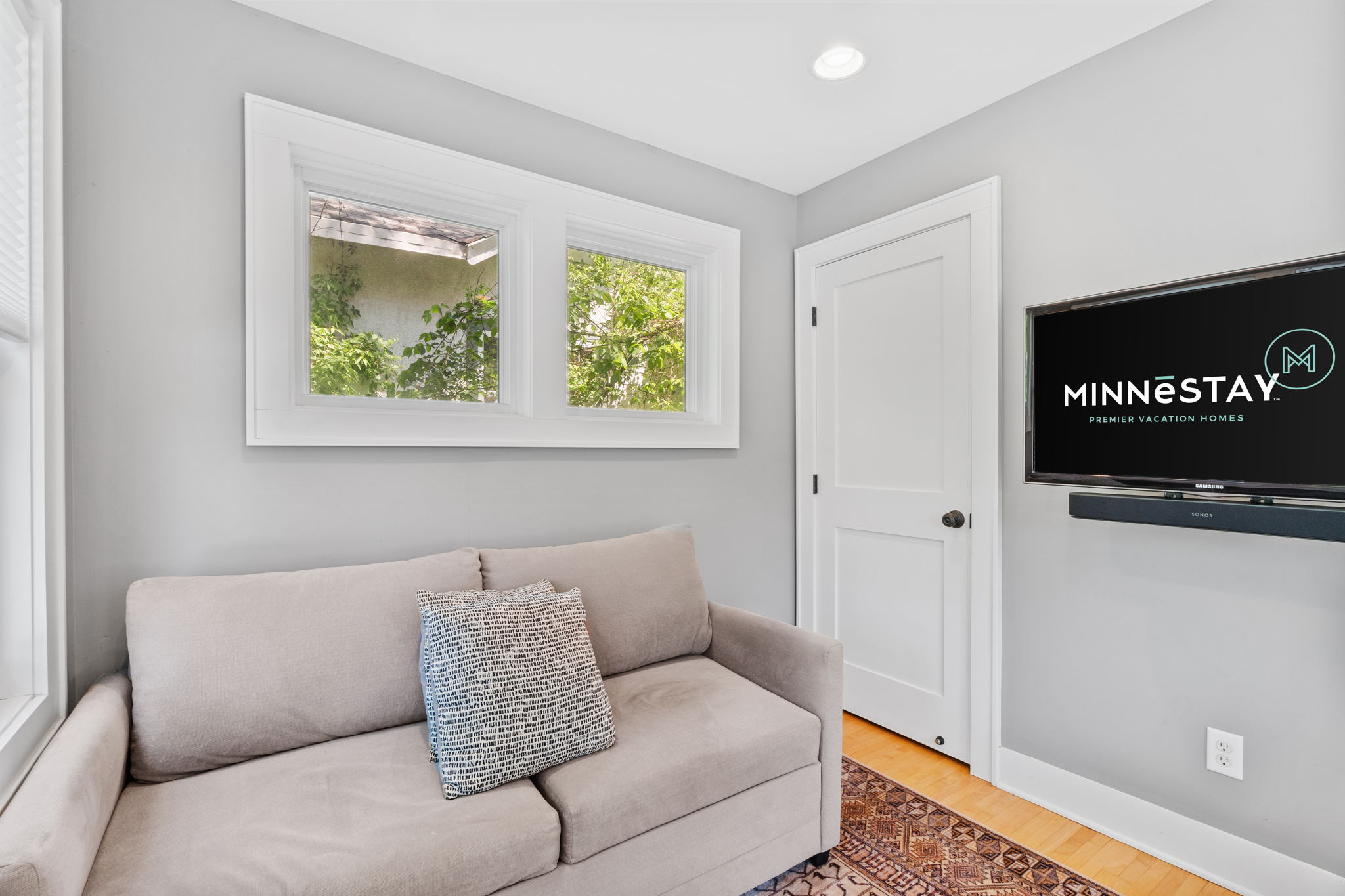 A cozy corner with modern decor, featuring a sofa, natural light, and a mounted TV.