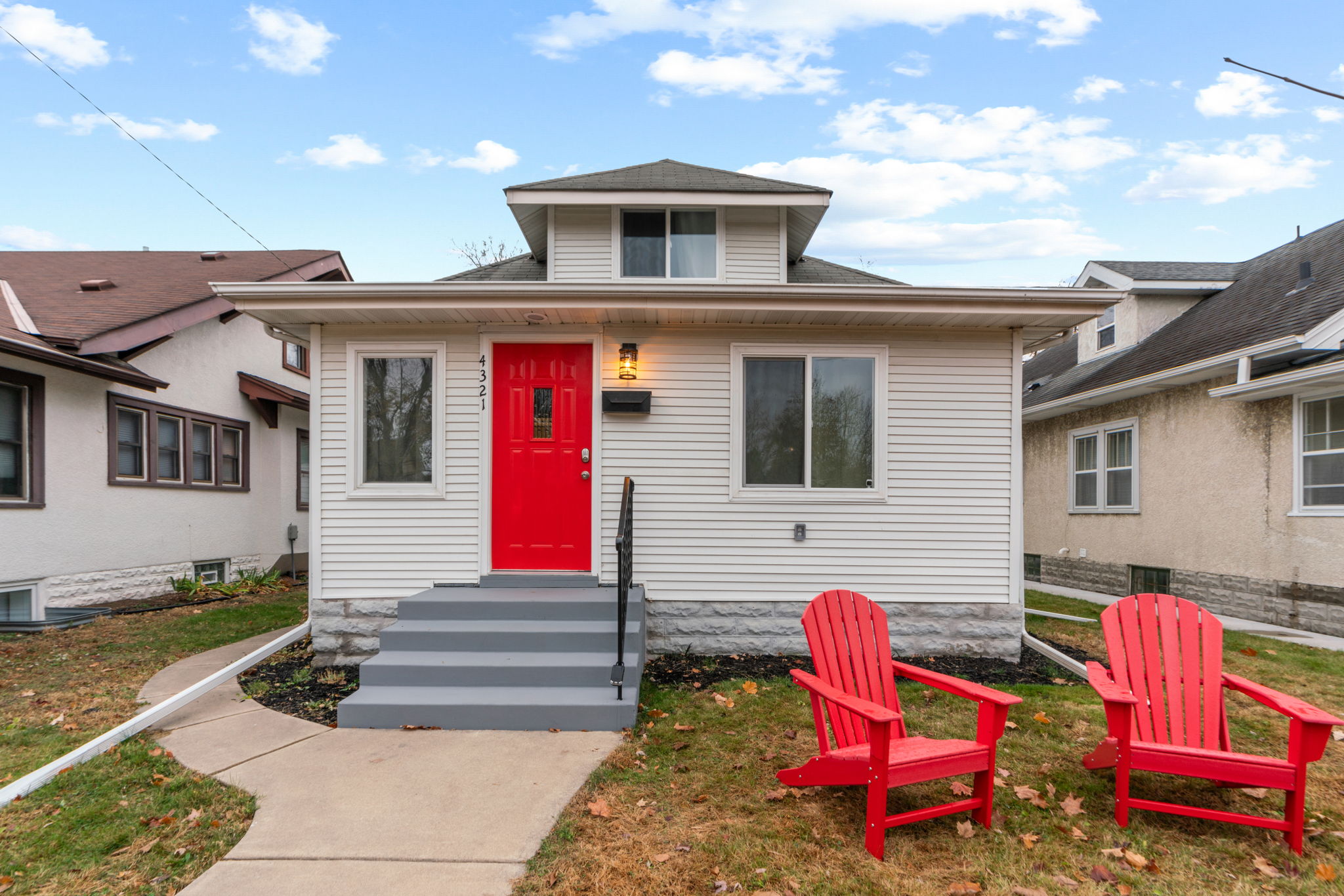 A charming home with a vibrant red door and inviting Adirondack chairs in the front yard.