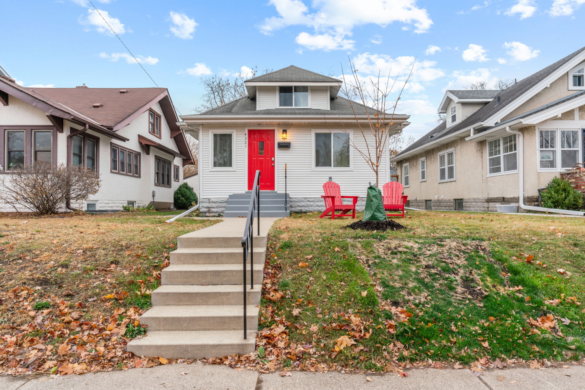 A cozy bungalow with a vibrant red door amidst autumn leaves.