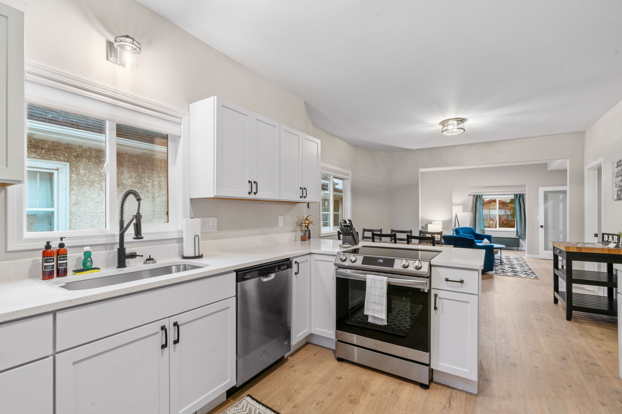 A modern kitchen with white cabinetry and stainless steel appliances, leading into a cozy living area.