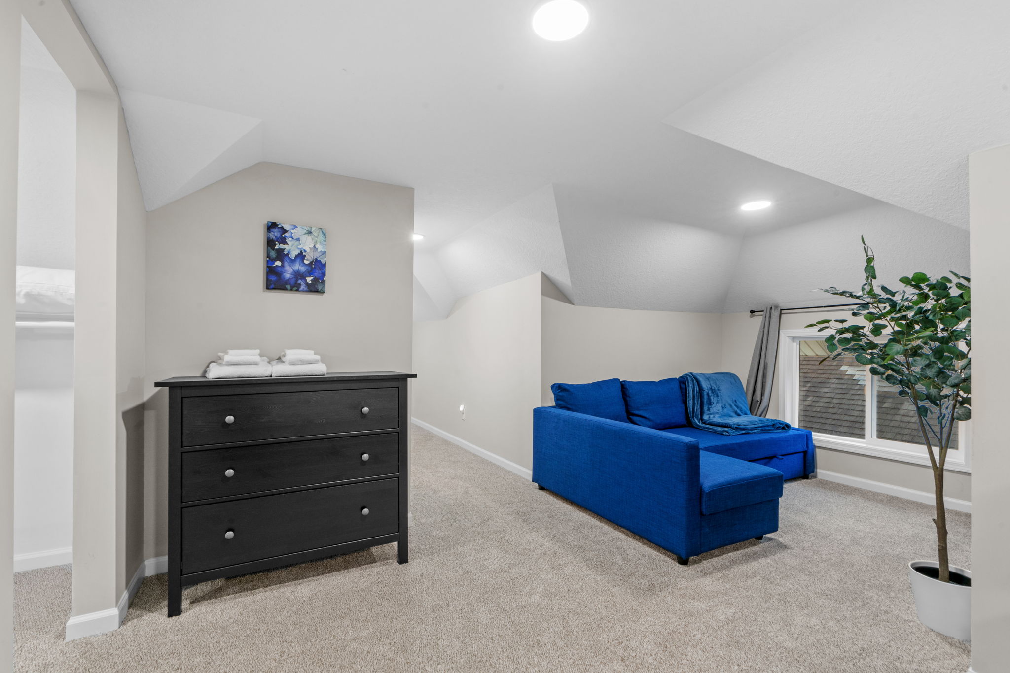 A serene attic room featuring a blue sofa, black dresser, and artistic decor.