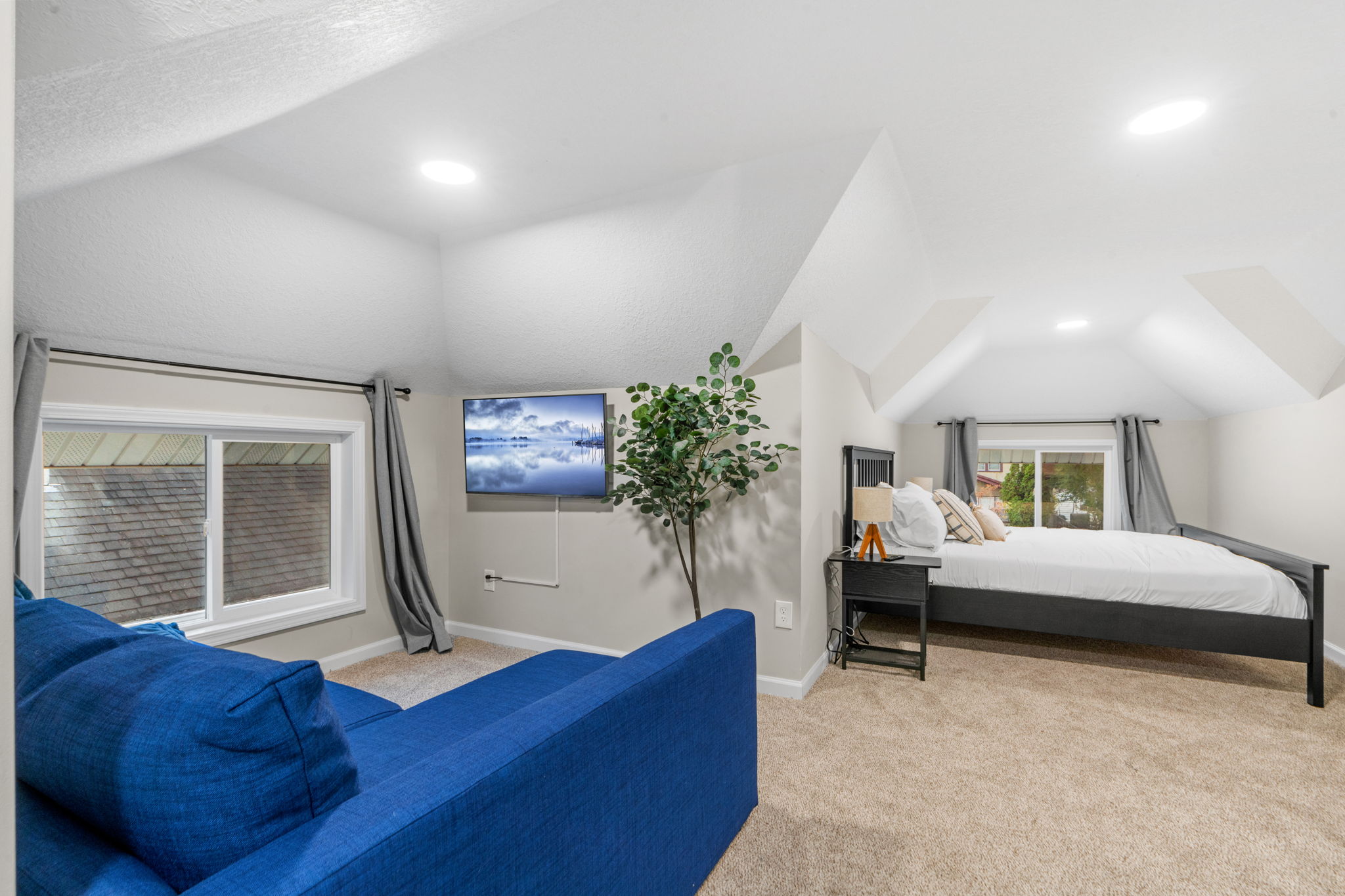 A cozy attic living space with a blue couch, bed, and modern amenities.