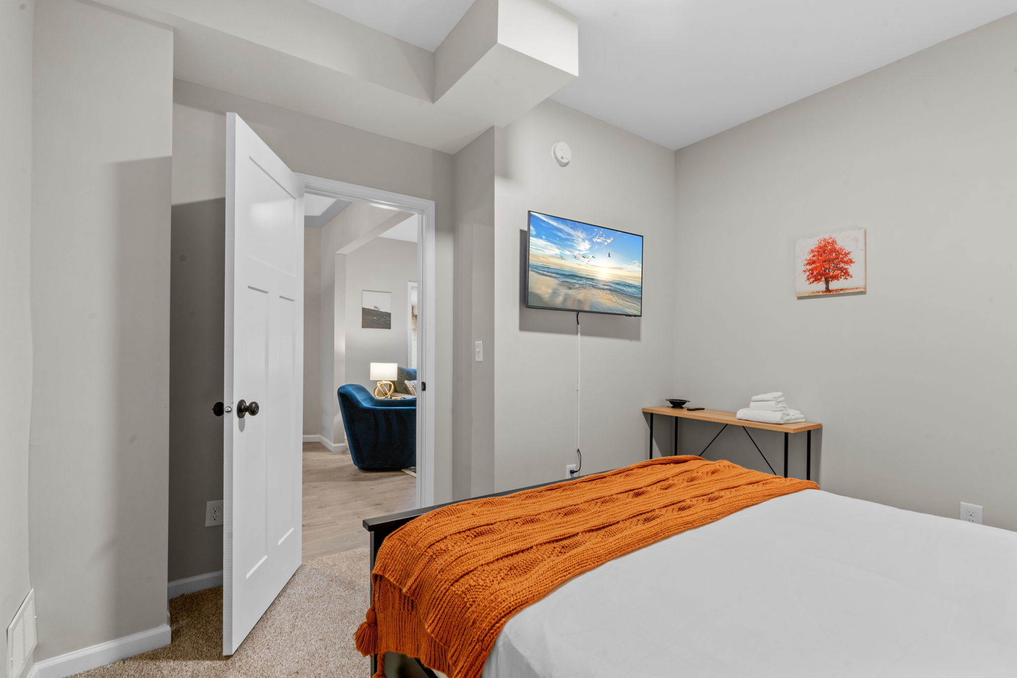 A modern bedroom featuring a cozy bed with an orange blanket and a mounted TV.