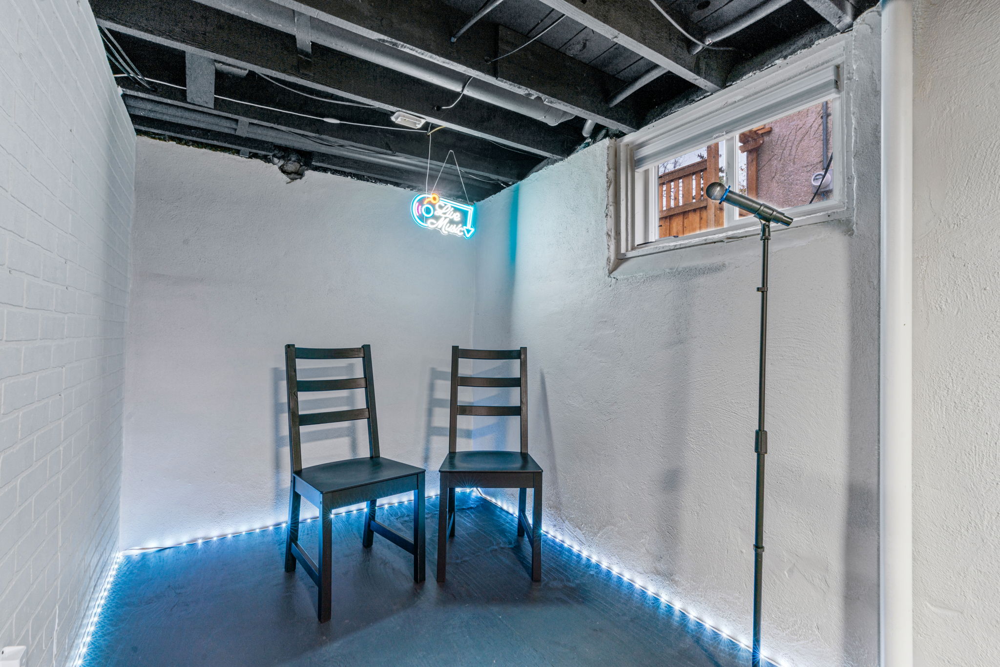 A cozy rehearsal space with chairs, a microphone, and a 'Live Music' neon sign.