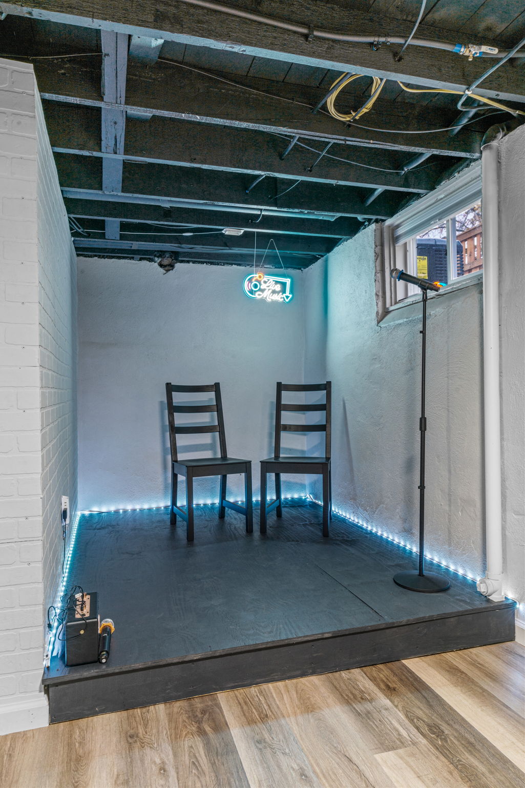 A cozy live music performance space with two chairs and a neon sign.