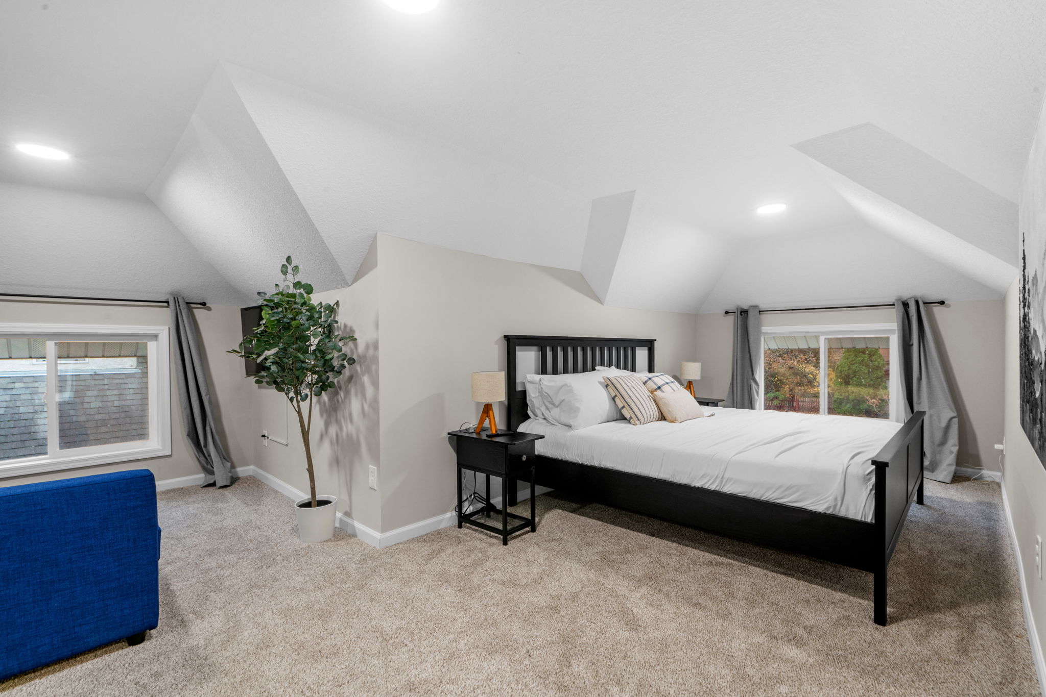 A cozy attic bedroom with a slanted ceiling, featuring a bed, a blue sofa, and a plant.