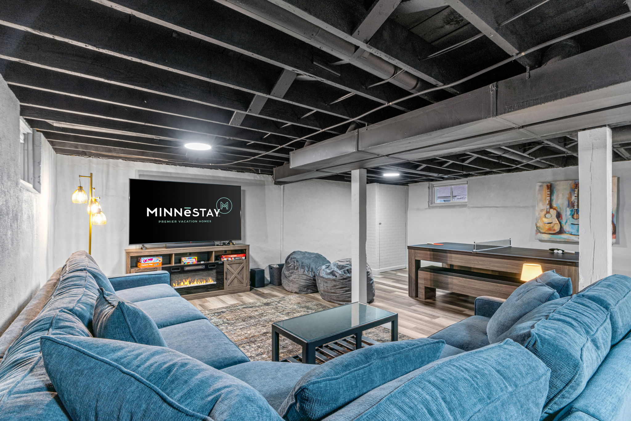 A modern basement living area featuring a cozy sectional sofa, entertainment setup, and ping-pong table.