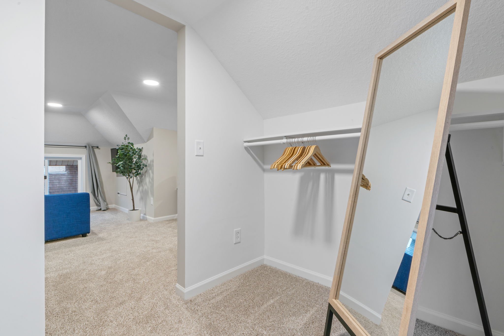 A stylish minimalistic walk-in closet area with a full-length mirror and wooden hangers.