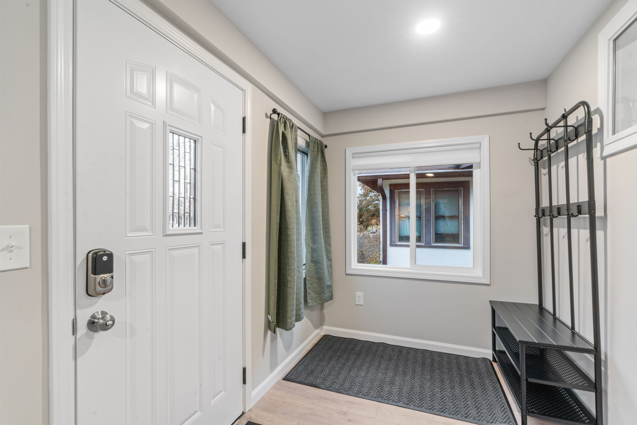 A modern and welcoming entryway featuring a white door and black coat rack.