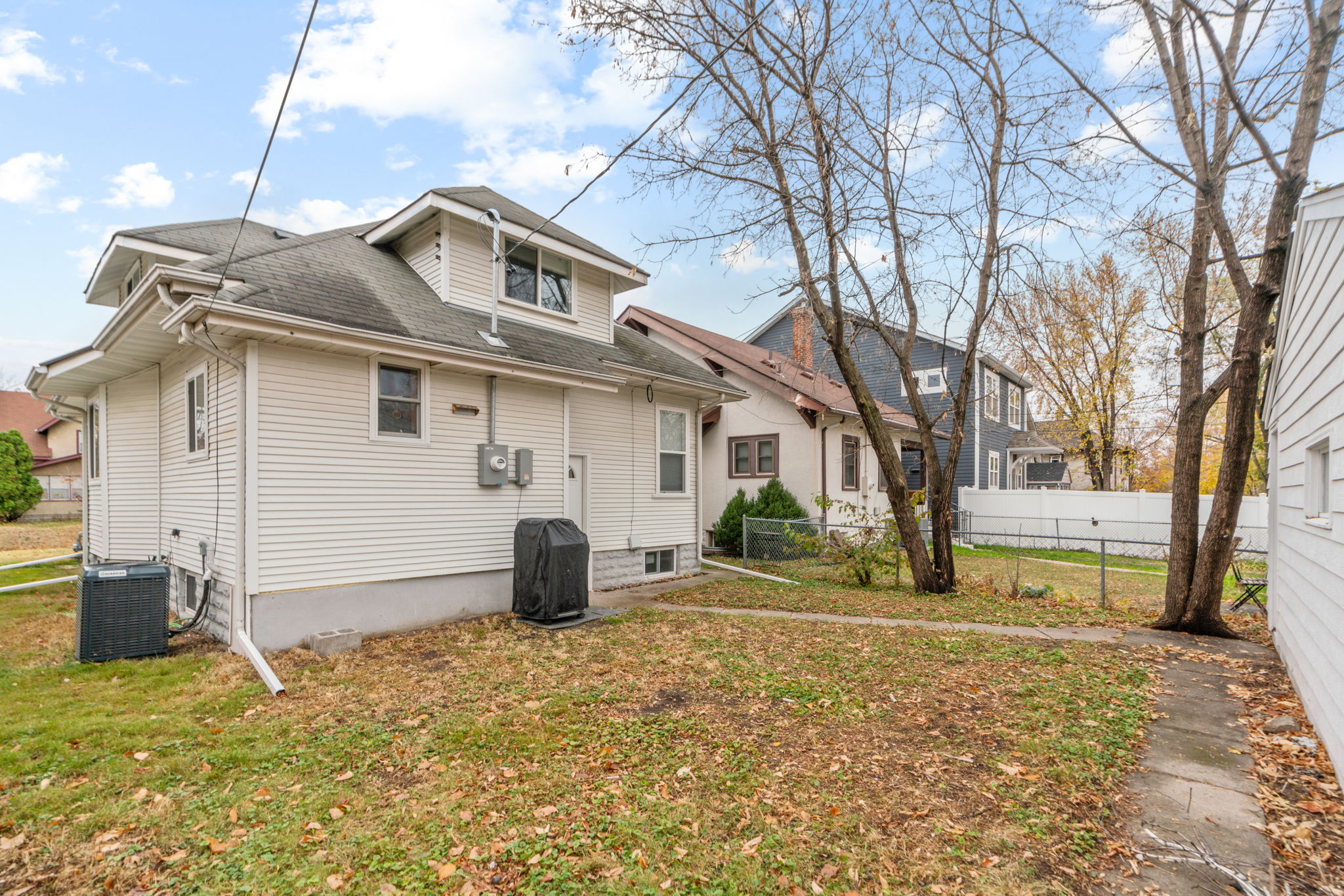 A side view of a suburban home in autumn, showcasing the backyard and neighboring houses.