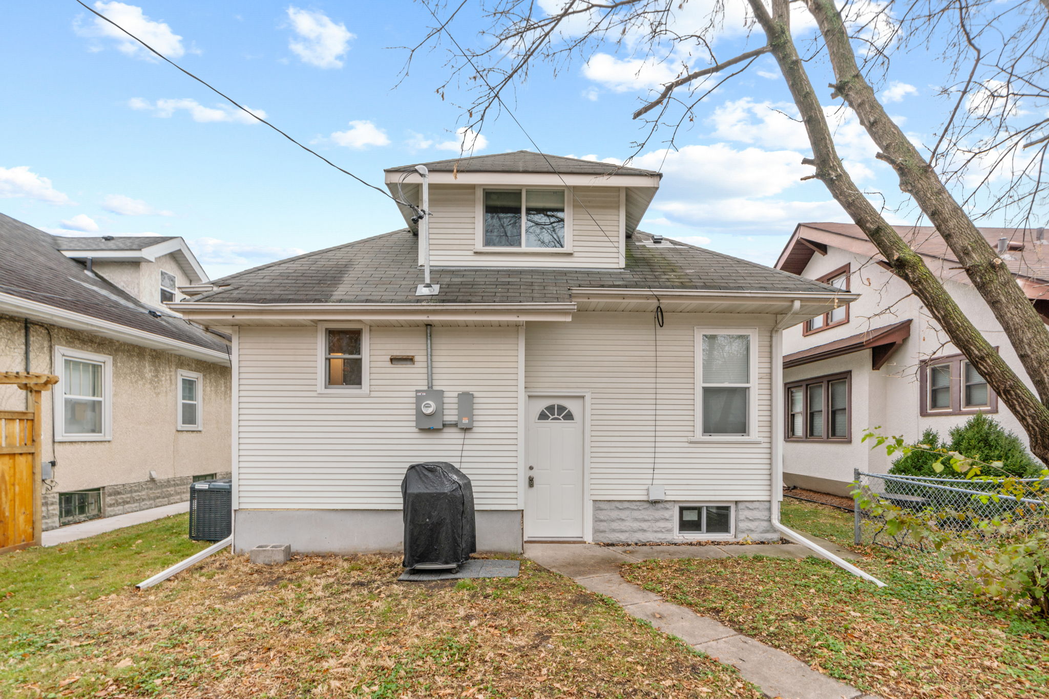 A charming two-story home with a small porch and a covered grill in the yard.