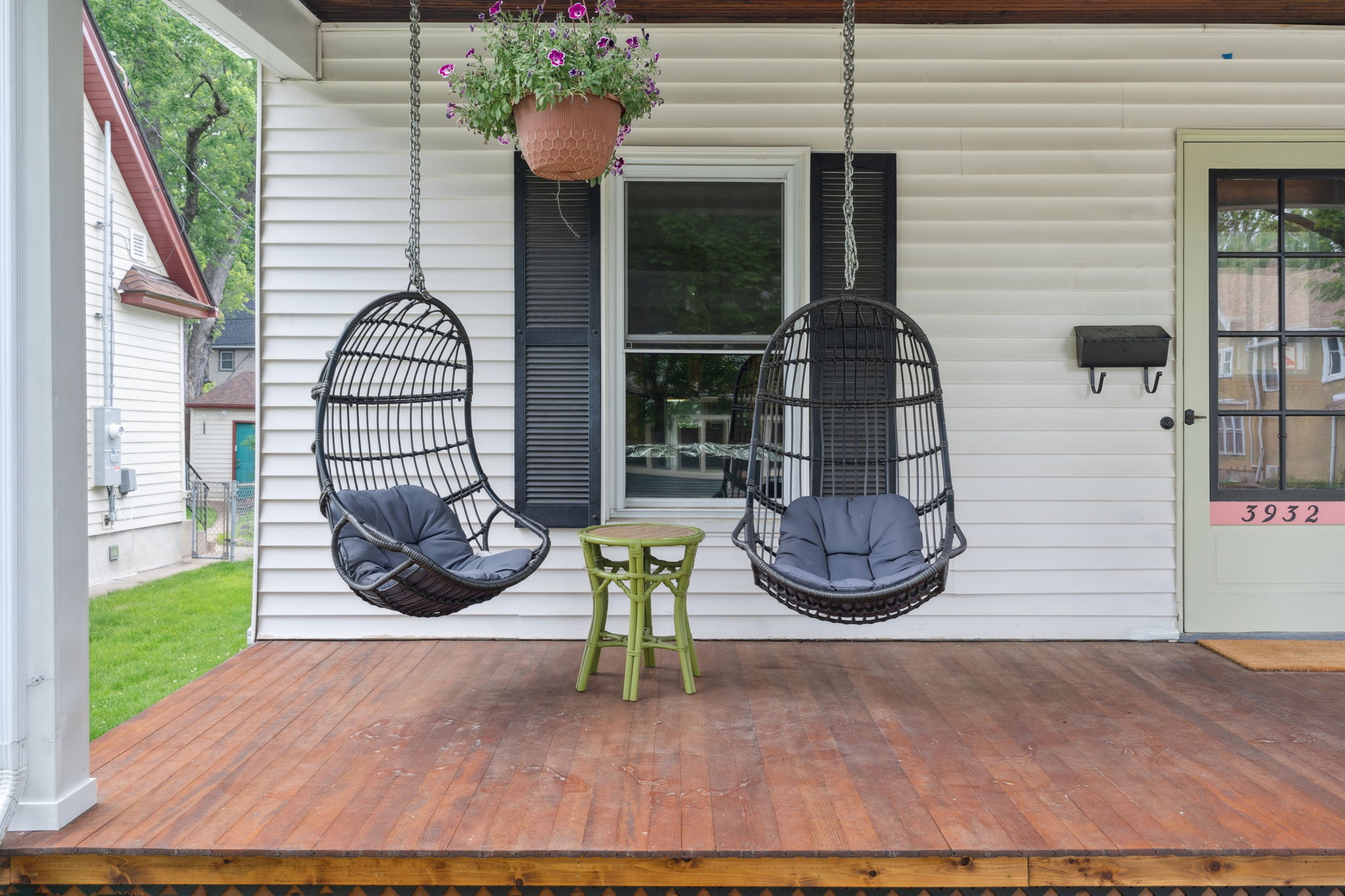 A cozy front porch with hanging wicker chairs and a small green stool.