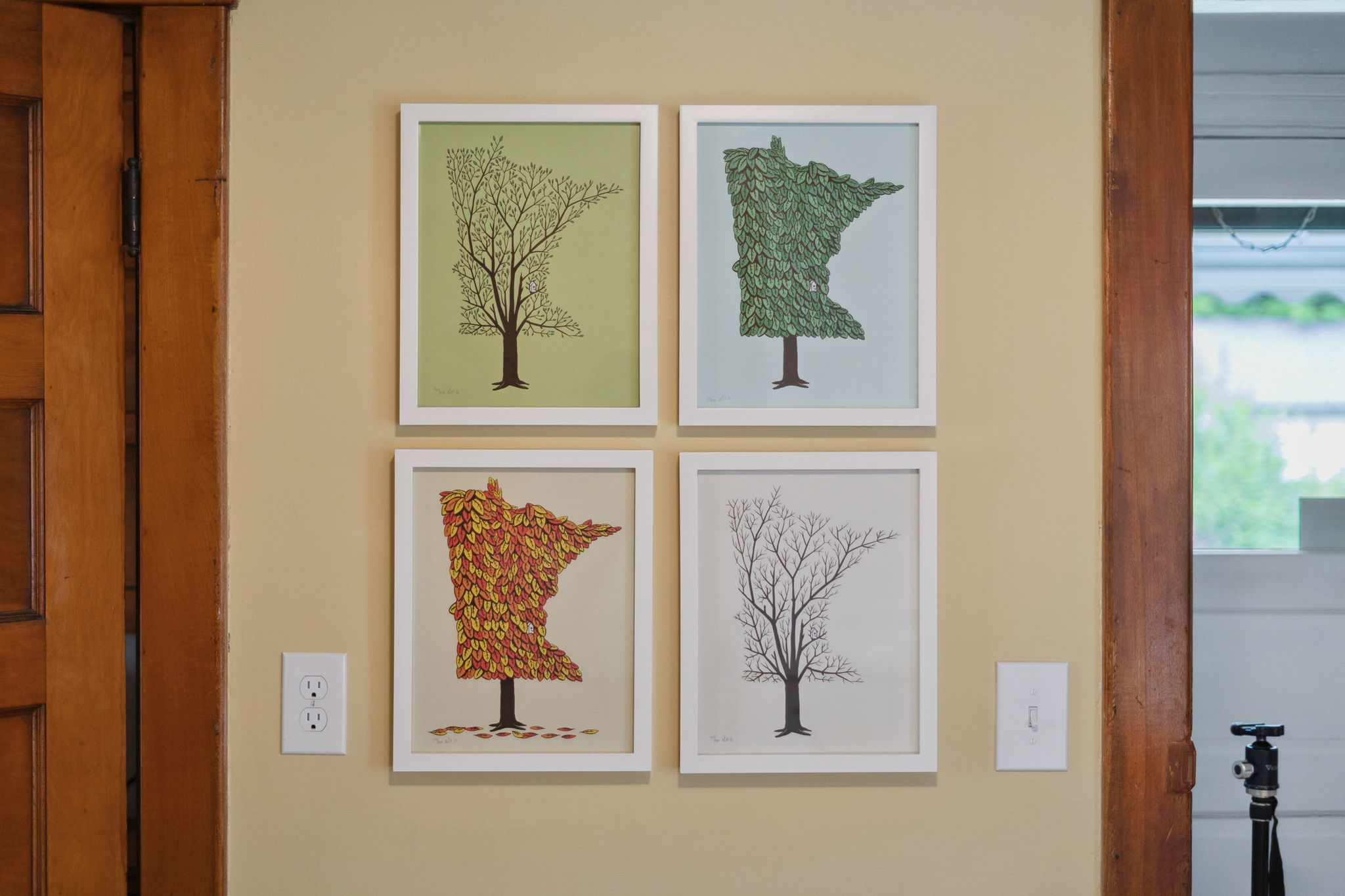 Four seasonal tree artworks framed on a beige wall.
