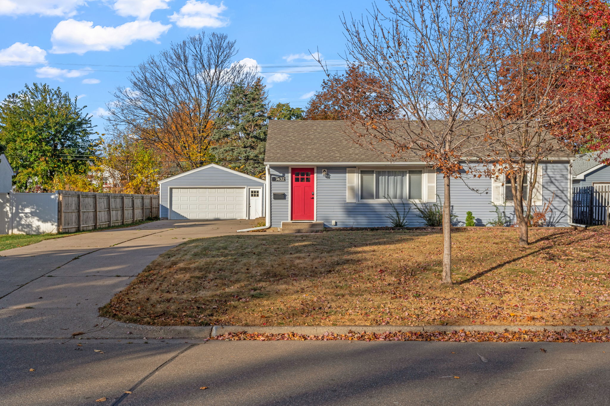 A charming single-story house with a red door and autumn scenery.