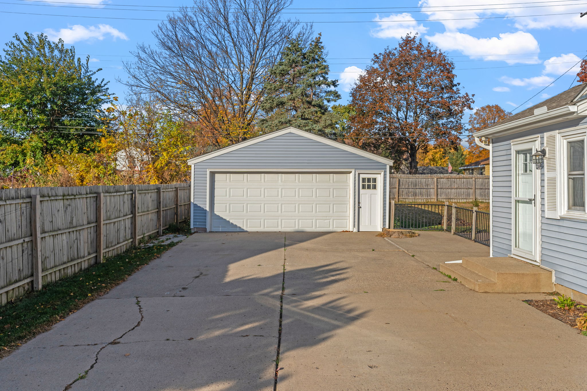 A serene driveway leading to a light blue garage, surrounded by autumn colors.