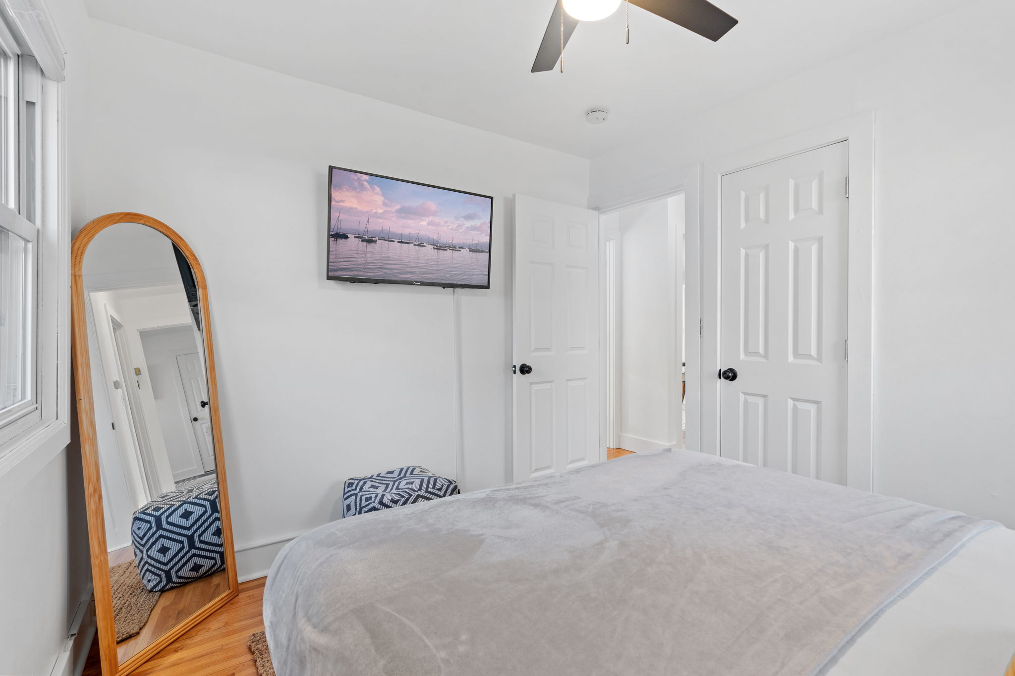 A serene bedroom featuring modern decor, a wall-mounted TV, and a tall mirror.
