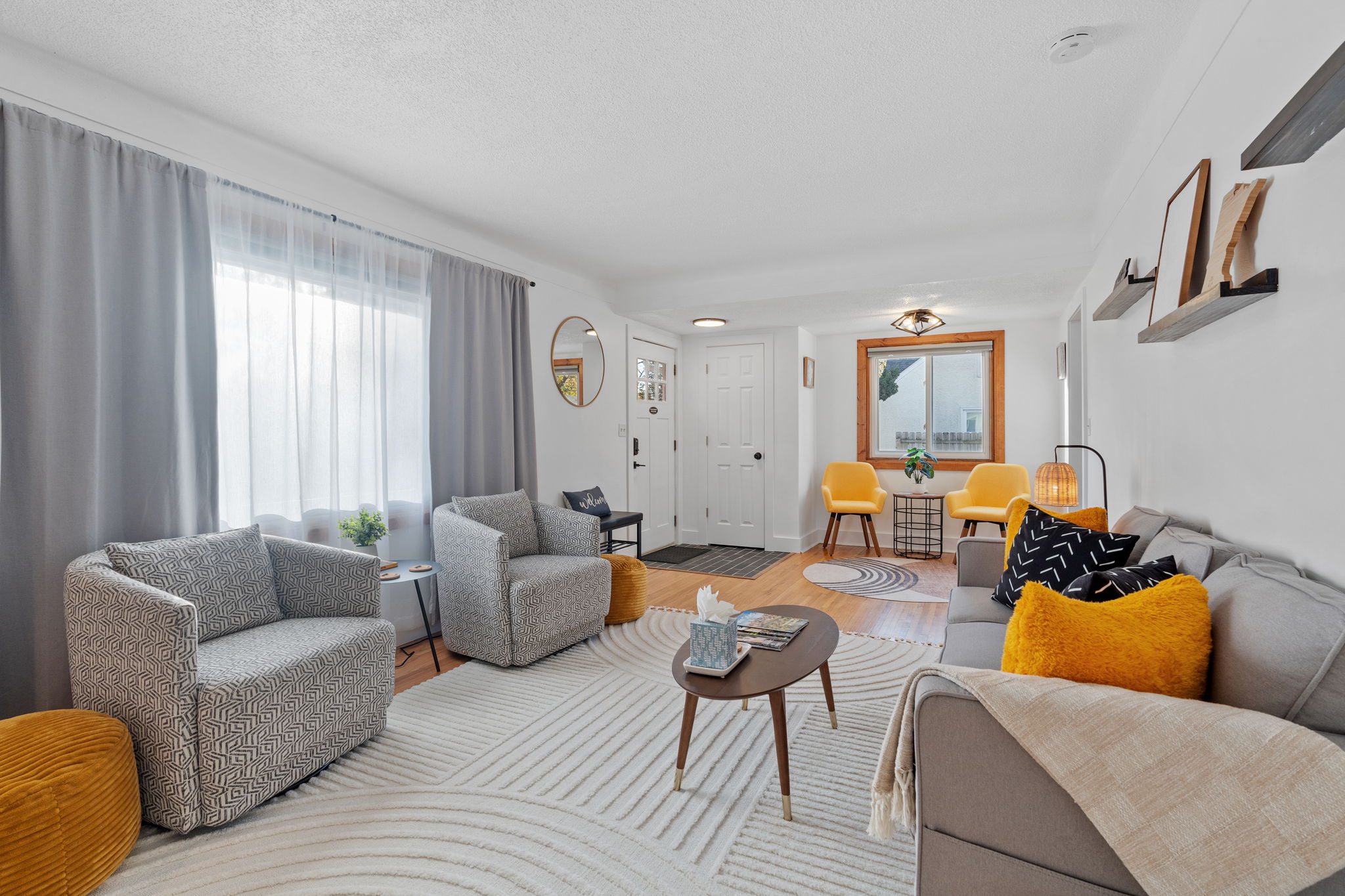 A cozy living room featuring a gray sofa, patterned armchairs, and bright yellow chairs, illuminated by natural light.