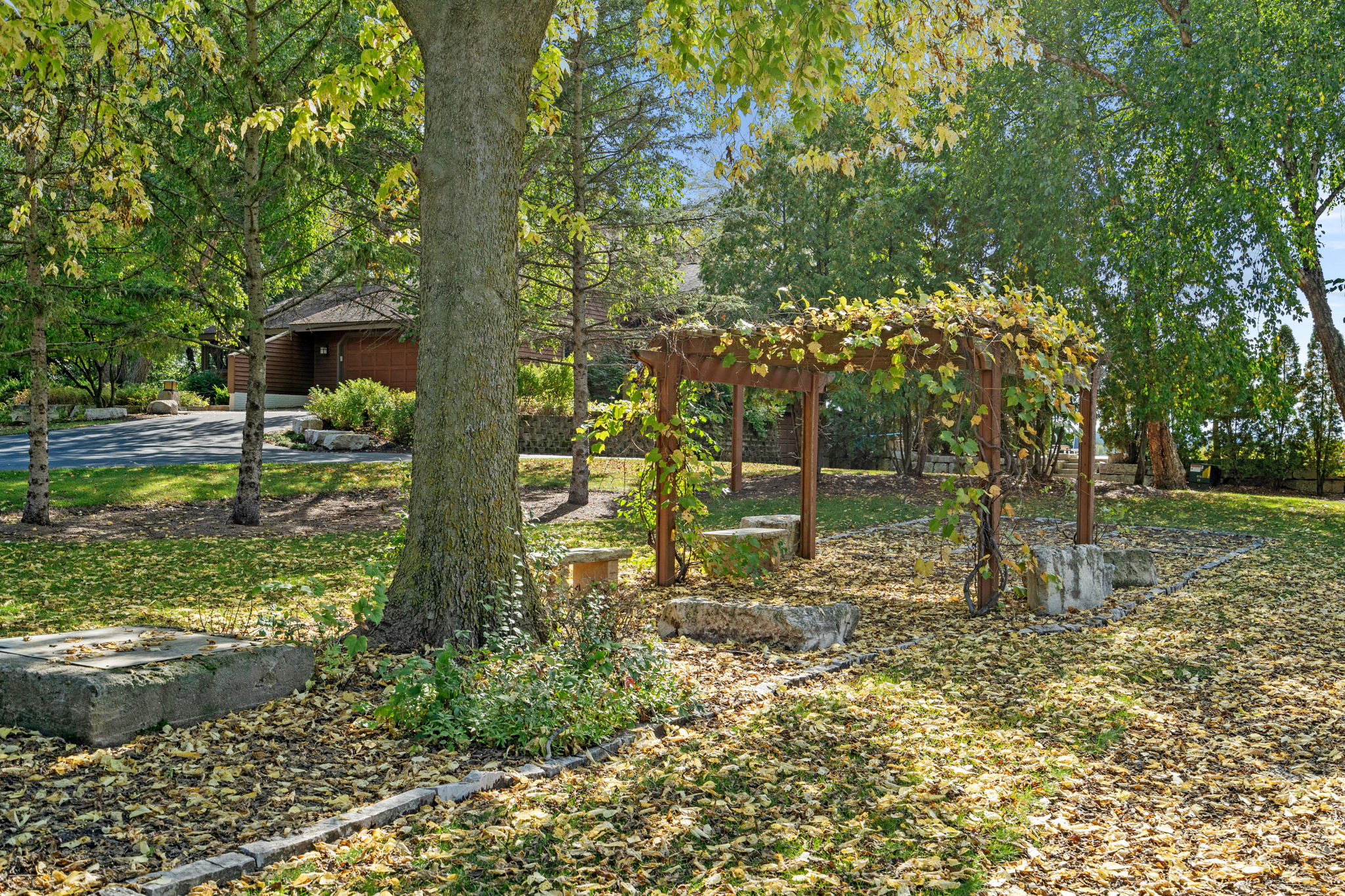 A tranquil autumn garden featuring a wooden gazebo and fallen leaves.