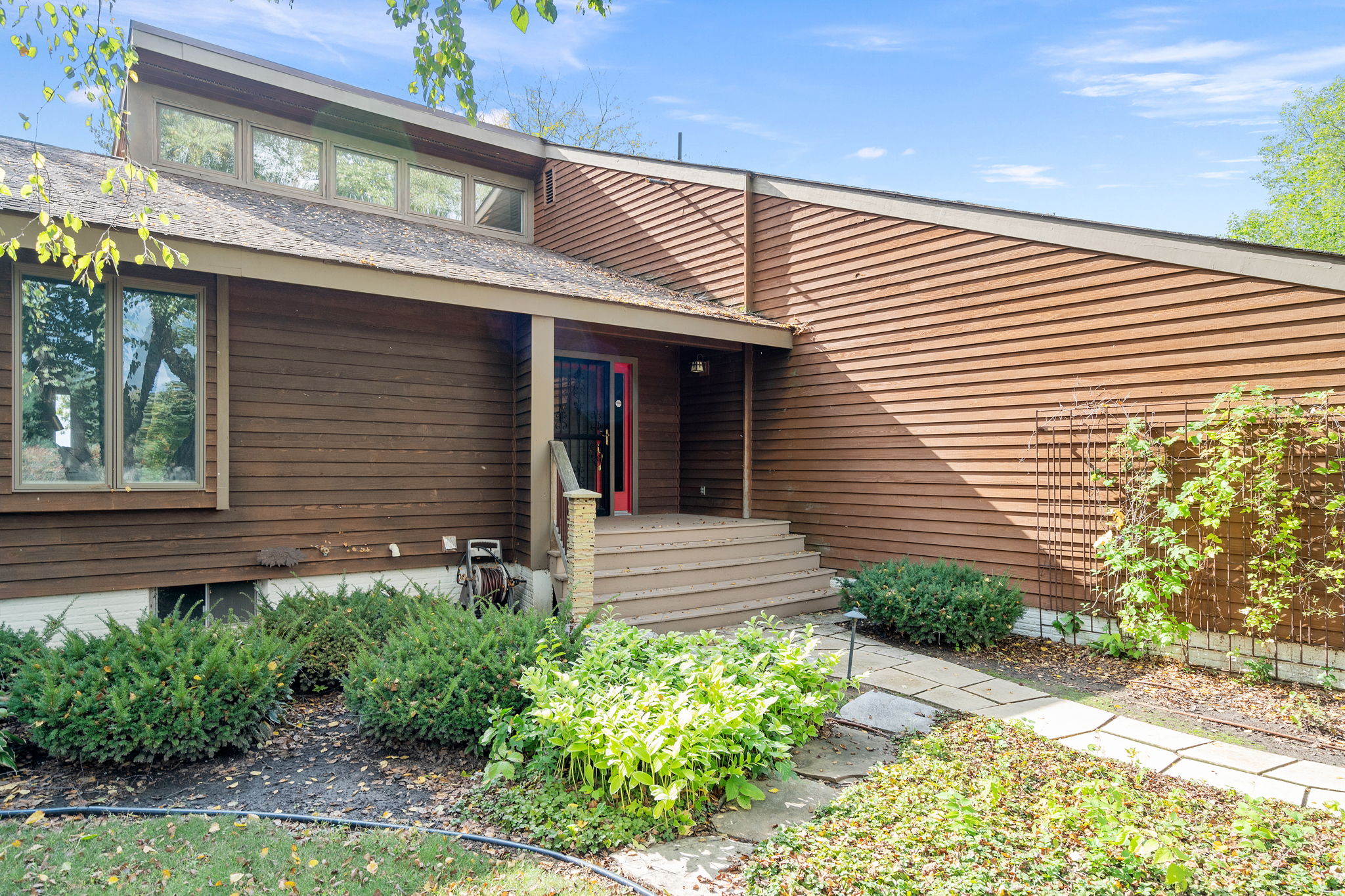 A modern wooden home with a pink front door surrounded by lush greenery.