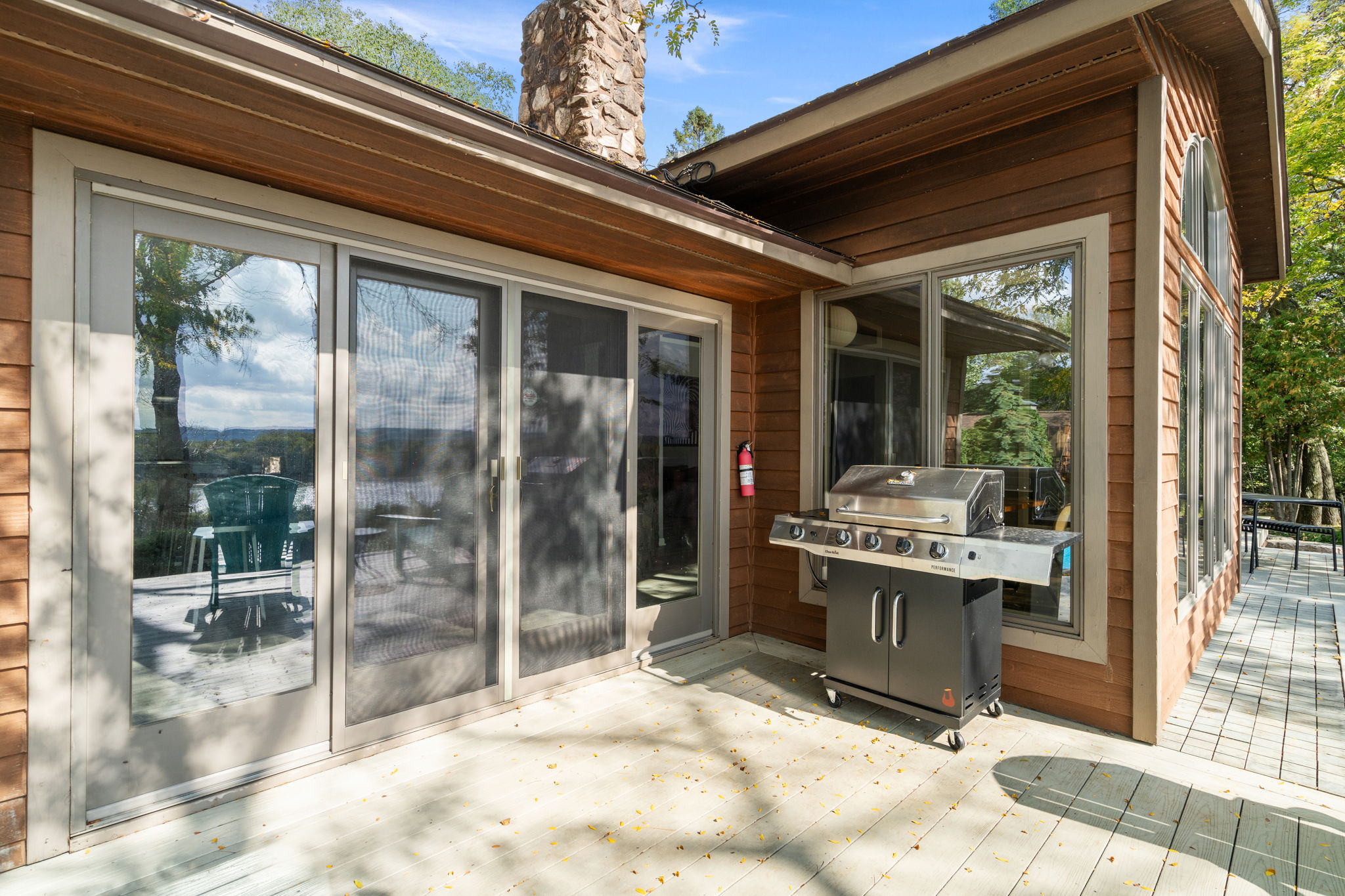 A modern outdoor space with a wooden deck and grill, featuring large glass doors and a stone chimney.