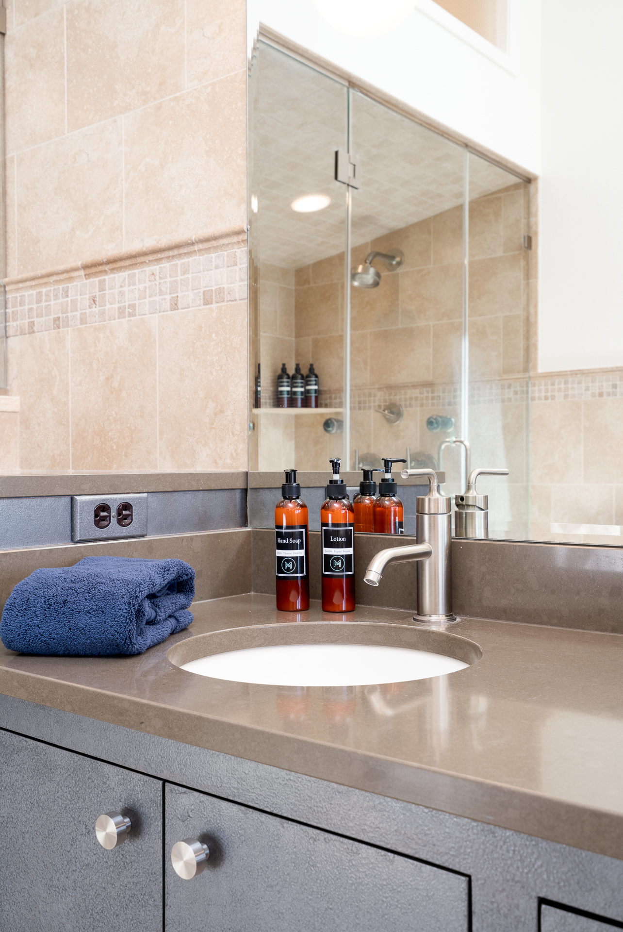 A stylish modern bathroom sink with elegant bottles and a folded towel.