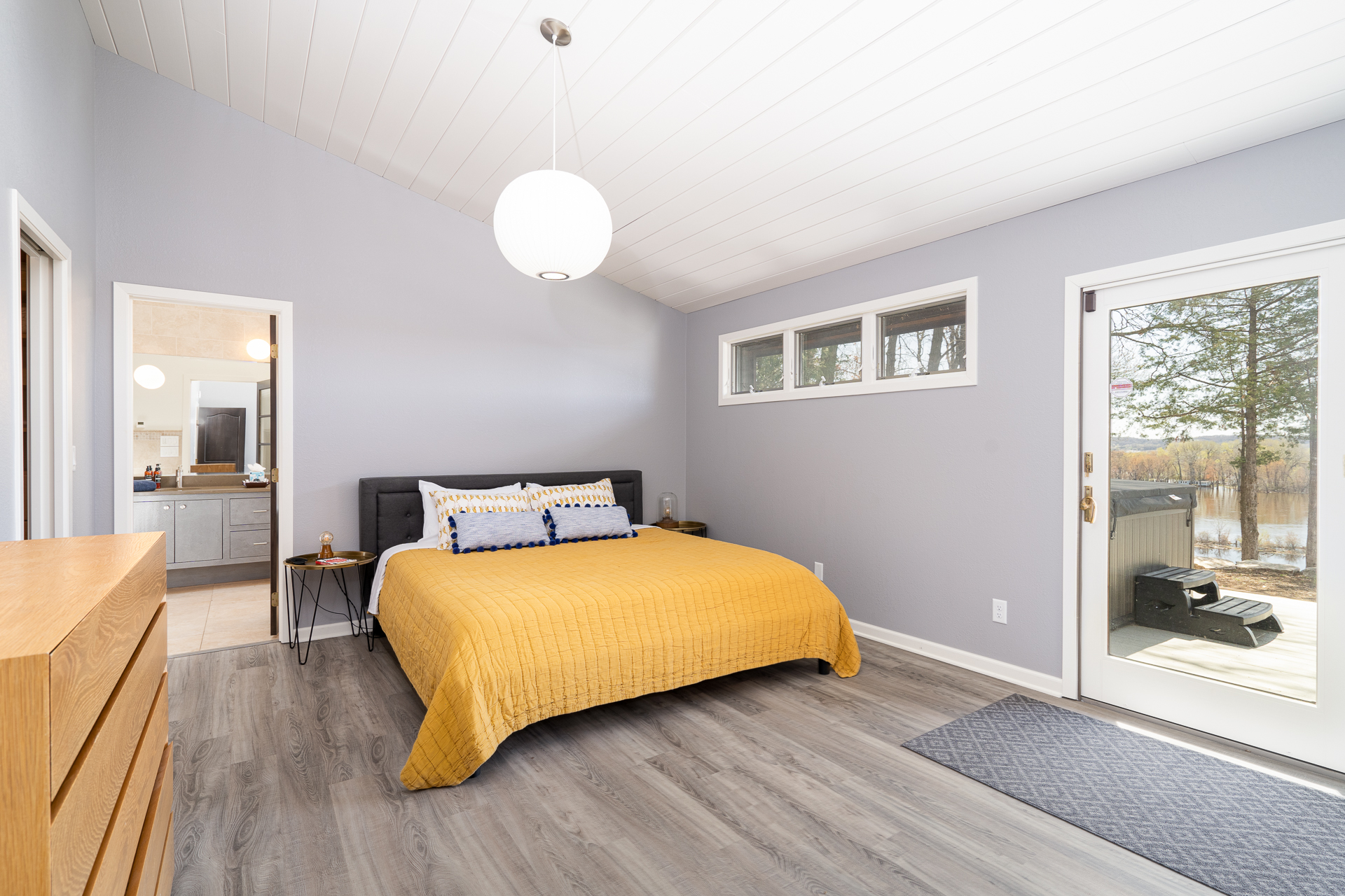A modern bedroom with a bright mustard quilt and serene outdoor views.