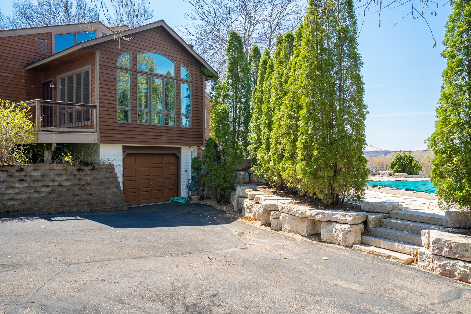 A contemporary wooden house with large windows and an inviting driveway, flanked by evergreen trees.