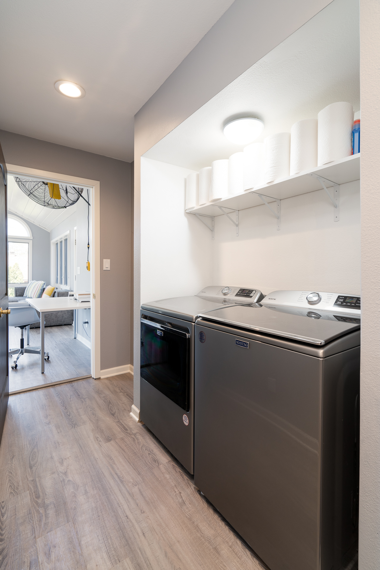 A modern laundry area featuring sleek washer and dryer machines and a connected workspace with natural light.