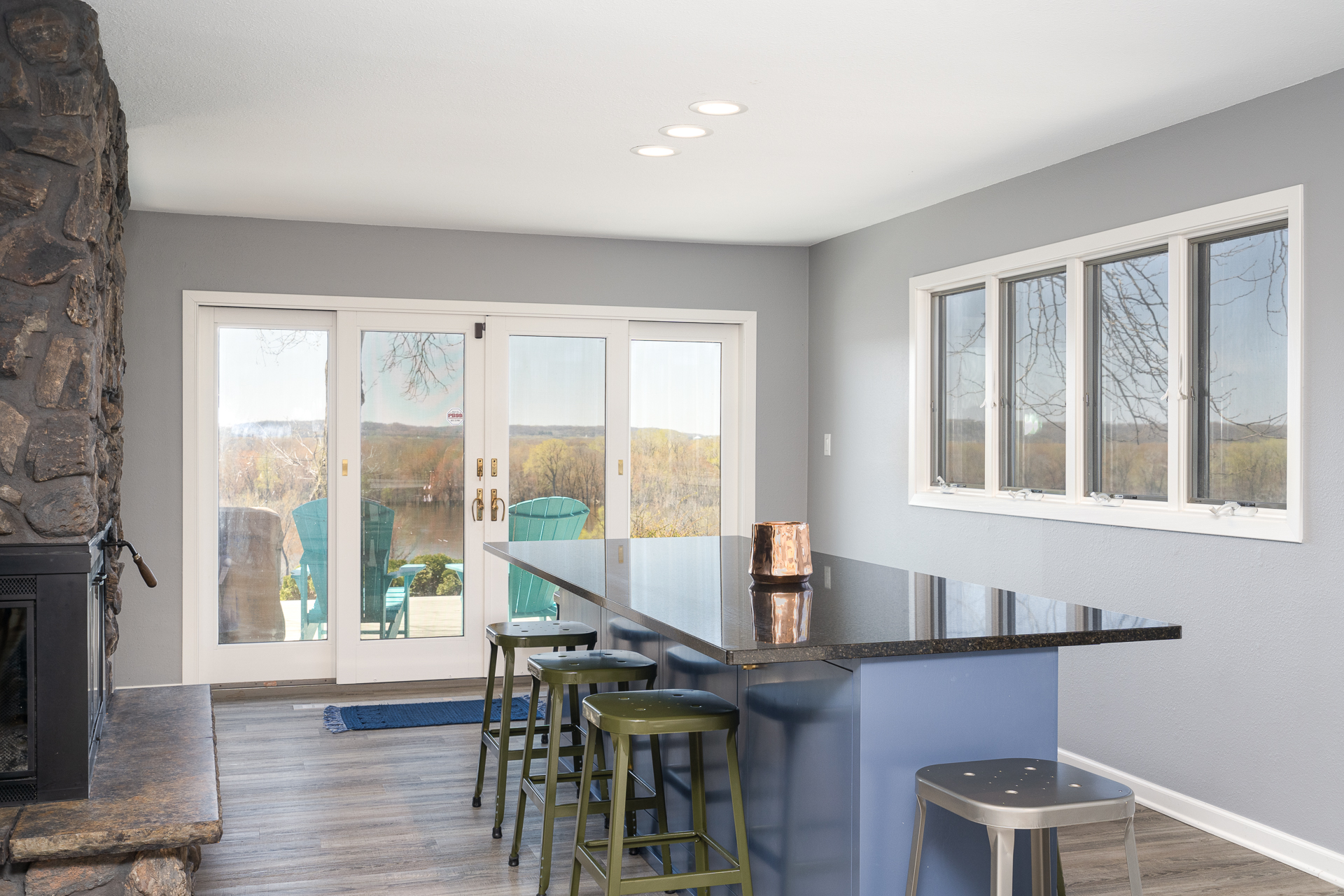 A modern kitchen with a stylish black counter and rustic stone fireplace, leading to a scenic outdoor view.