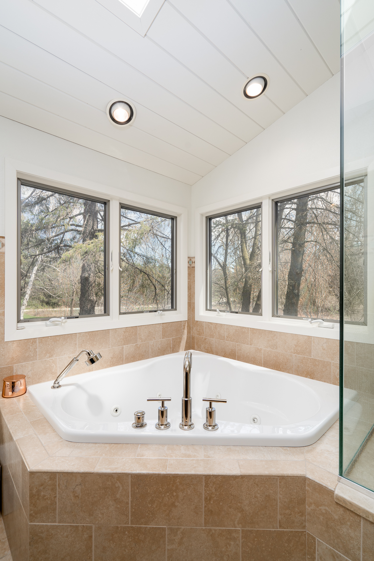 Modern corner bathtub surrounded by large windows and natural light.
