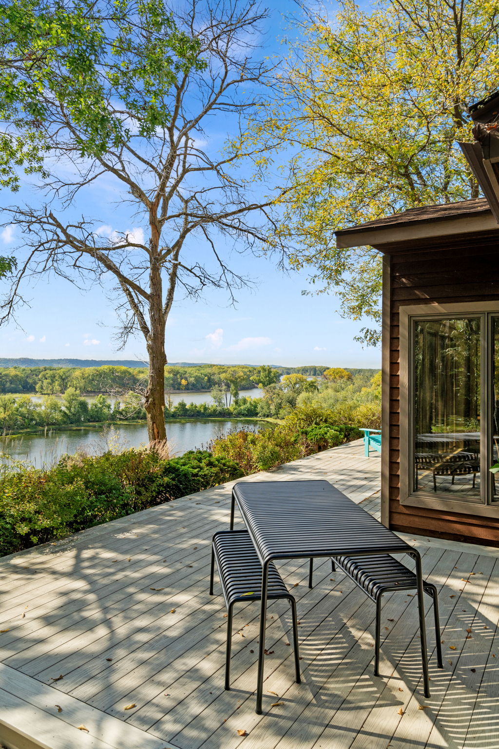 A tranquil riverside deck with a black metal table and chairs amid a beautiful autumn landscape.
