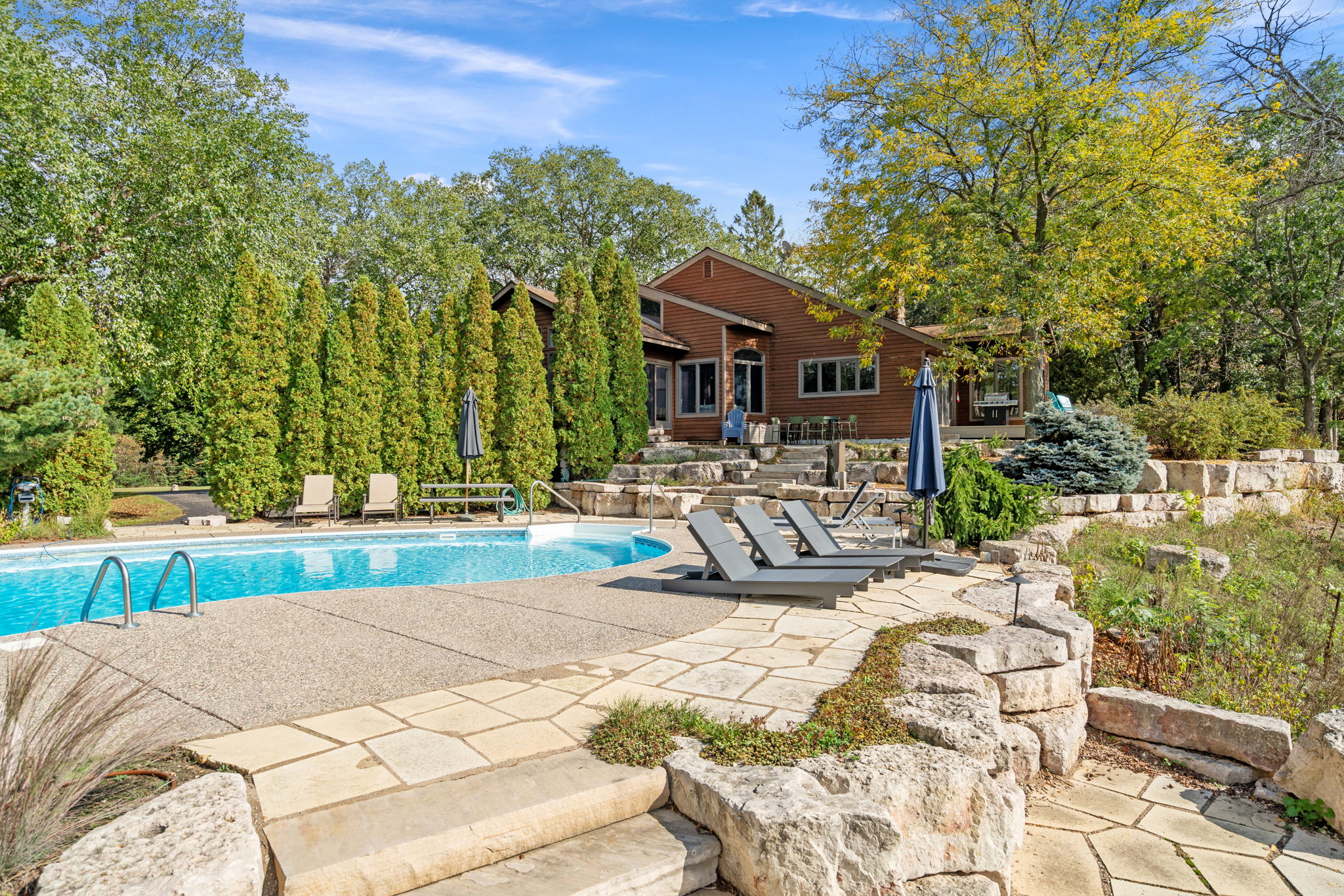 A tranquil outdoor pool area with modern lounge chairs and a cozy wooden house in the background.