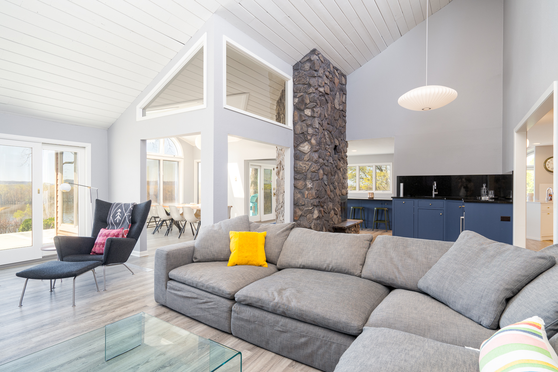A modern living room featuring high ceilings, a stone fireplace, and stylish furnishings.
