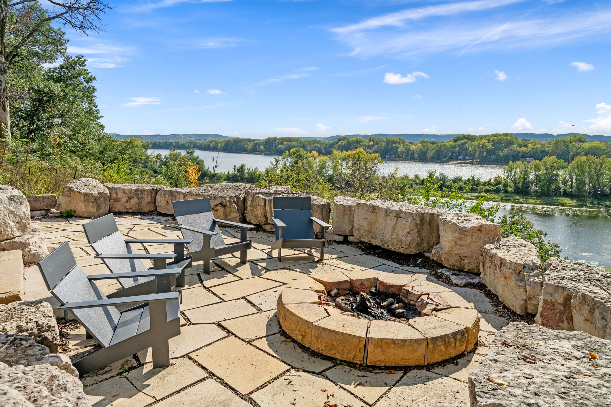 Modern chairs arranged around a fire pit with a picturesque river view.