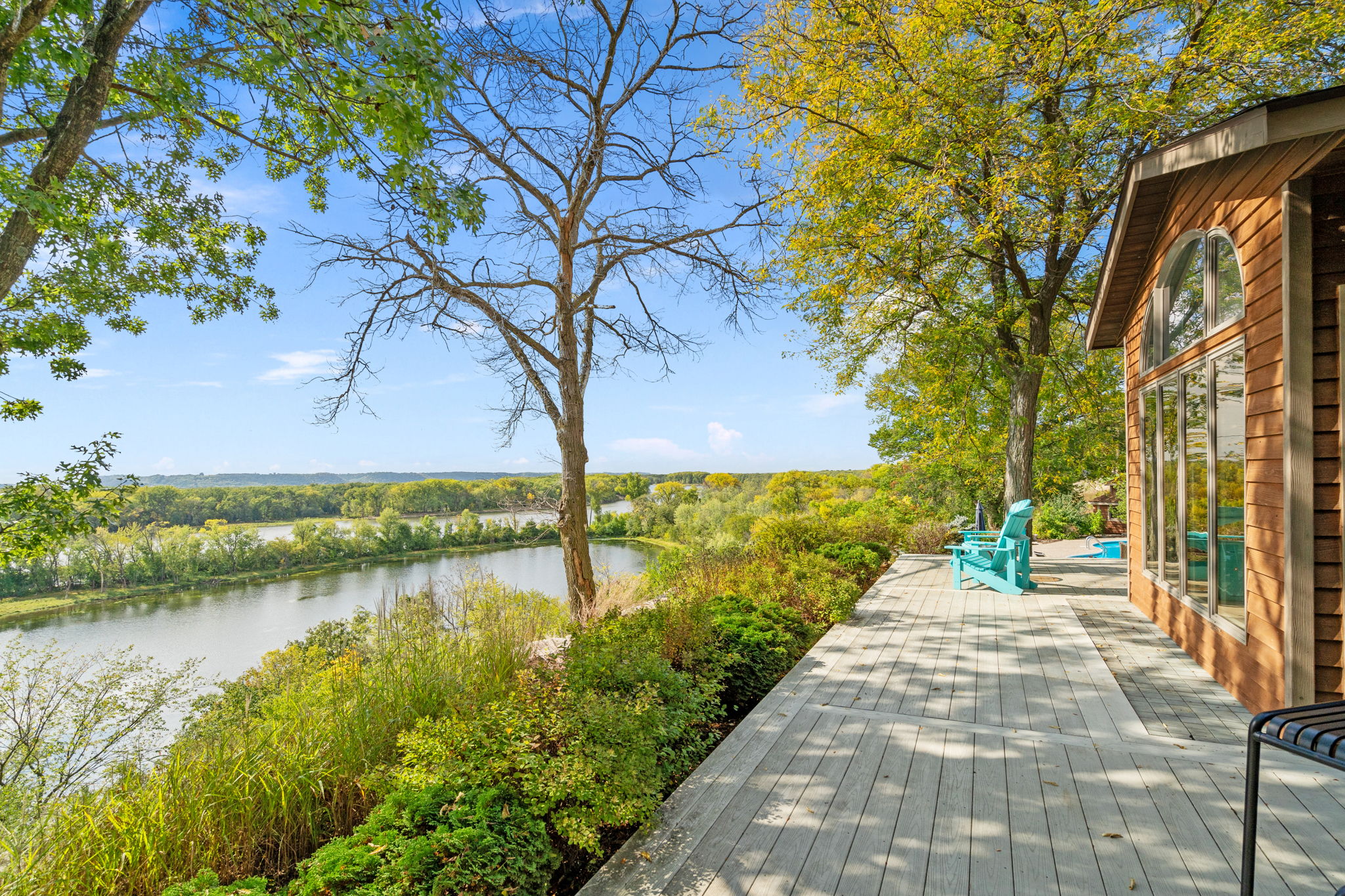 A serene riverside view from a cozy wooden deck adorned with autumn foliage.